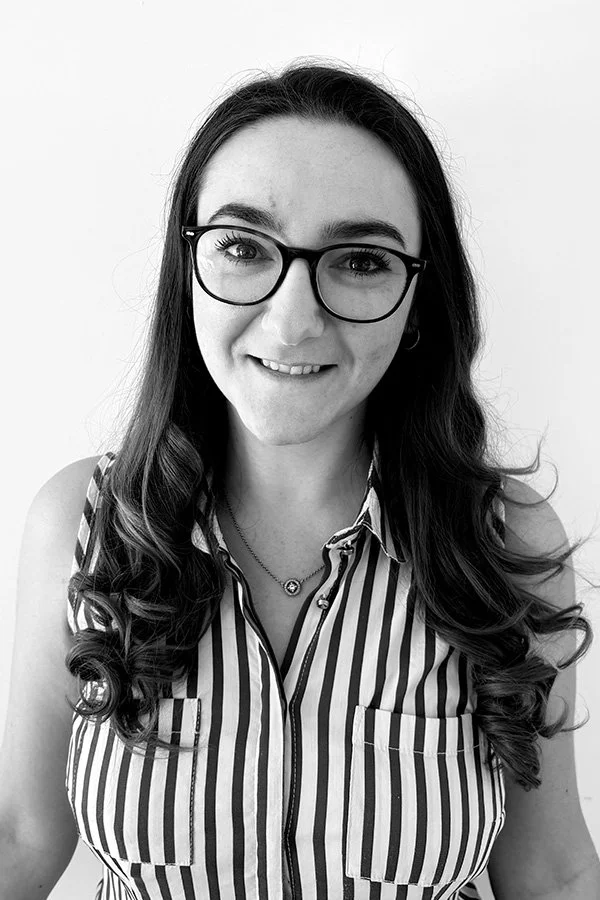A woman with long dark hair, glasses, and a striped sleeveless shirt smiling at the camera.