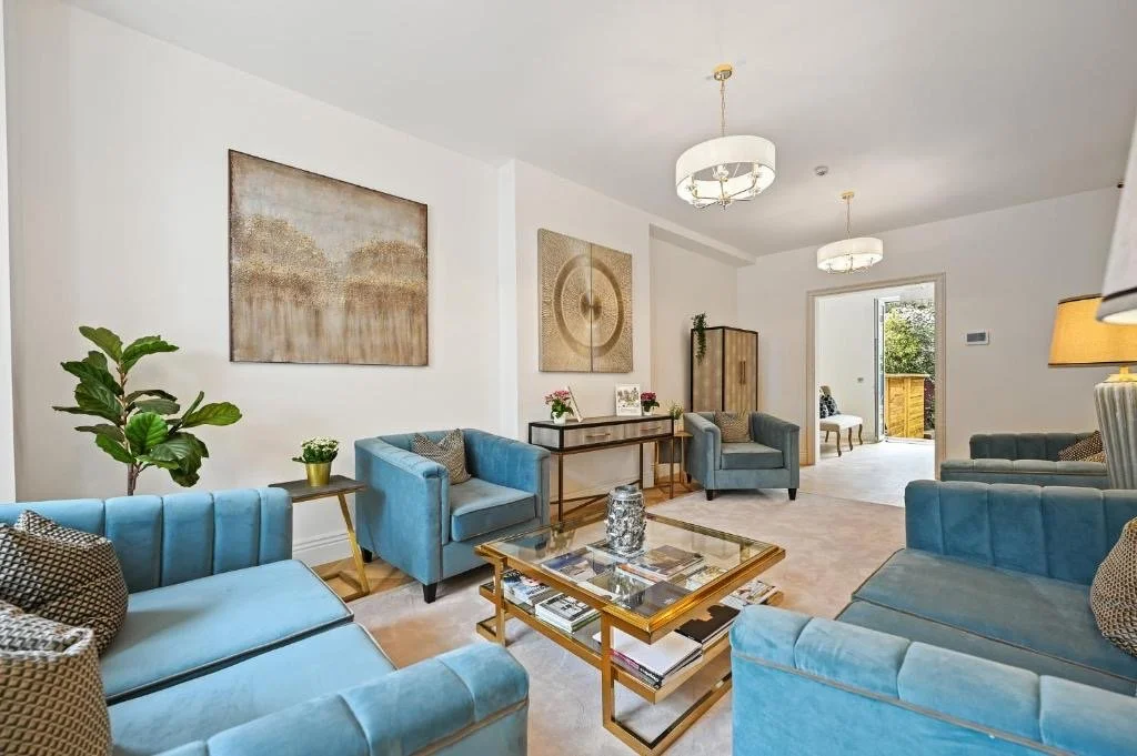 Living room with blue sofas, glass coffee table, modern artwork, and indoor plants.