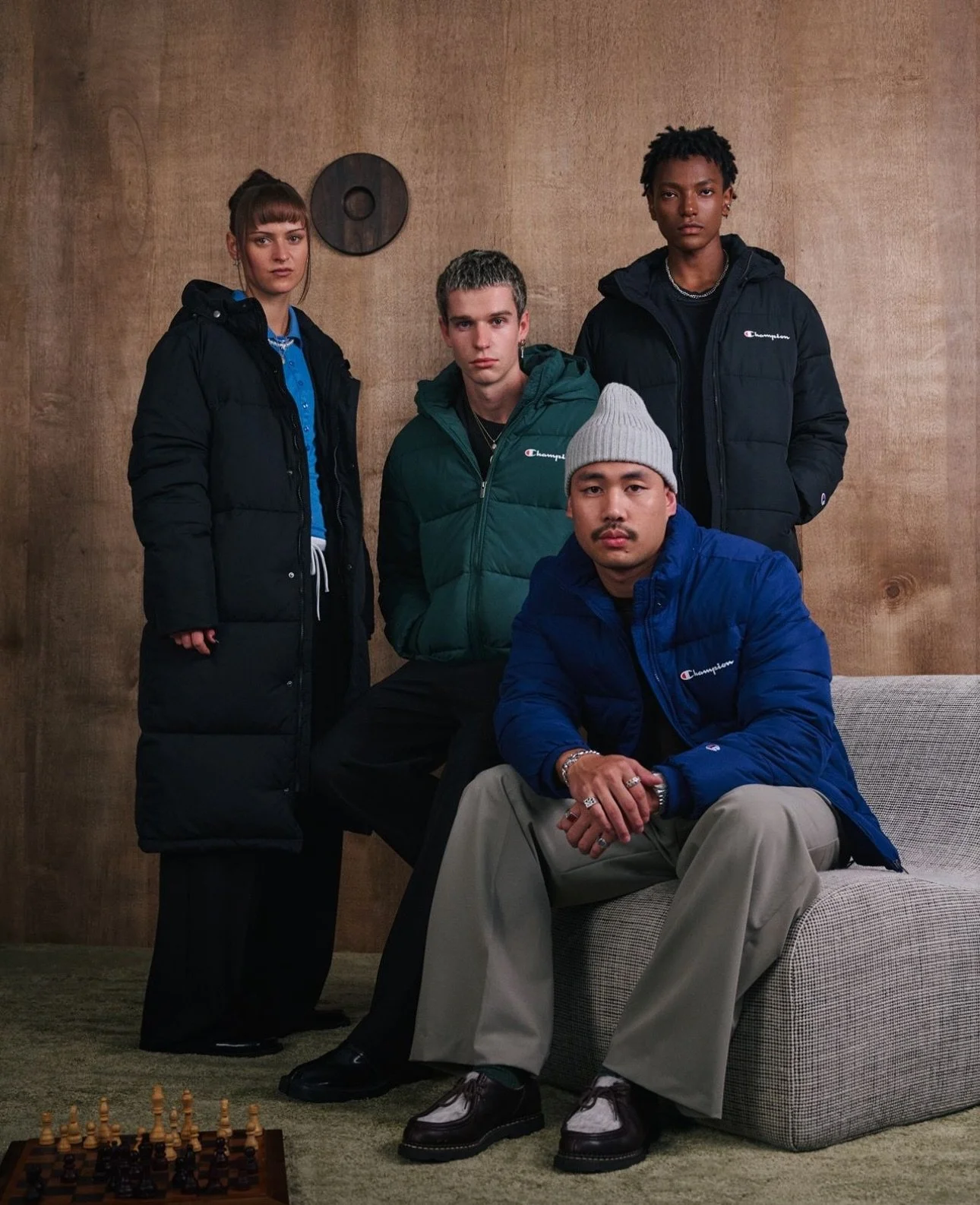 Champion campaign photograph of four models wearing jackets against a warm timber backdrop.