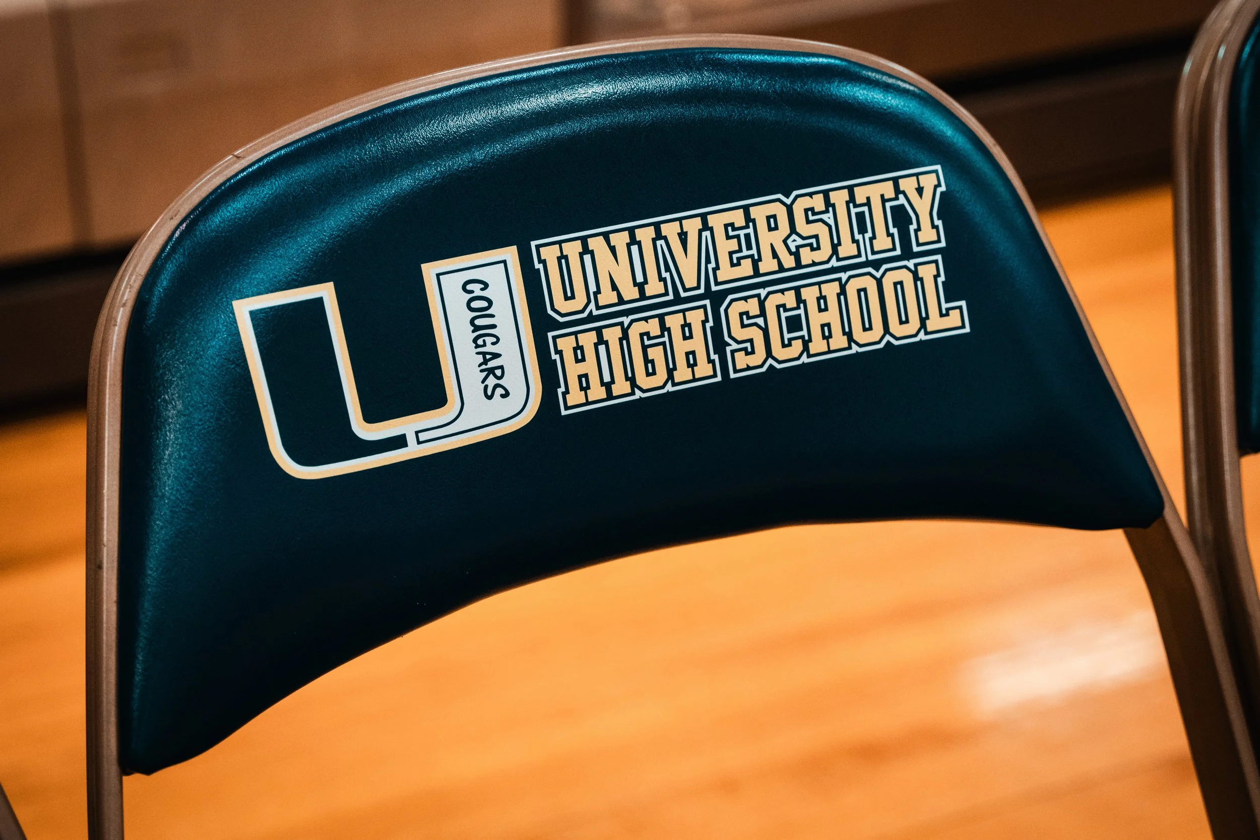 A black chair with a sticker that reads "Cougars" and "University High School" in gold and white lettering.