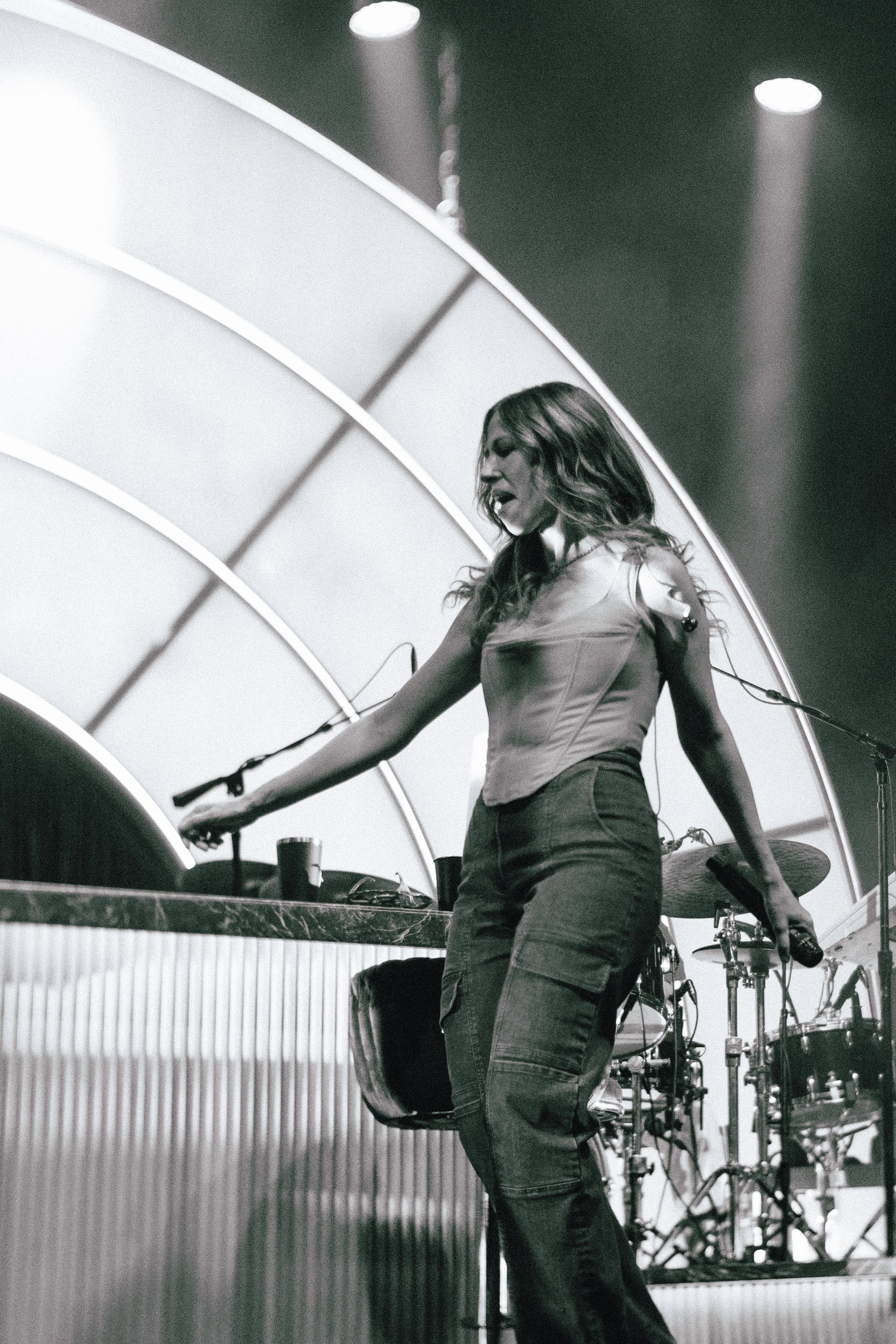Female musician performing on stage at a concert, playing the keyboard, with drums in the background.