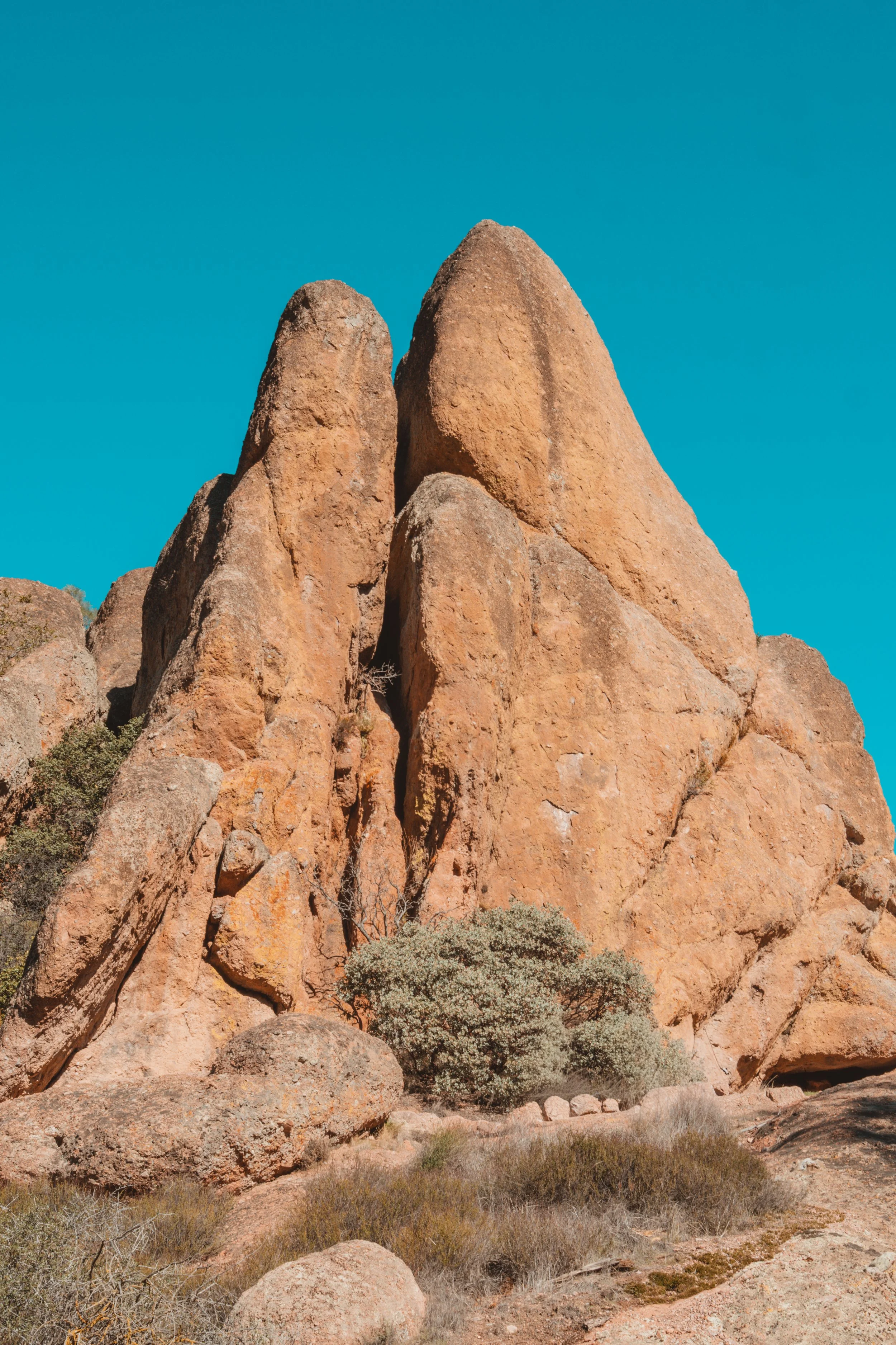 Large reddish-brown rock formations against a clear blue sky with sparse desert vegetation at their base.