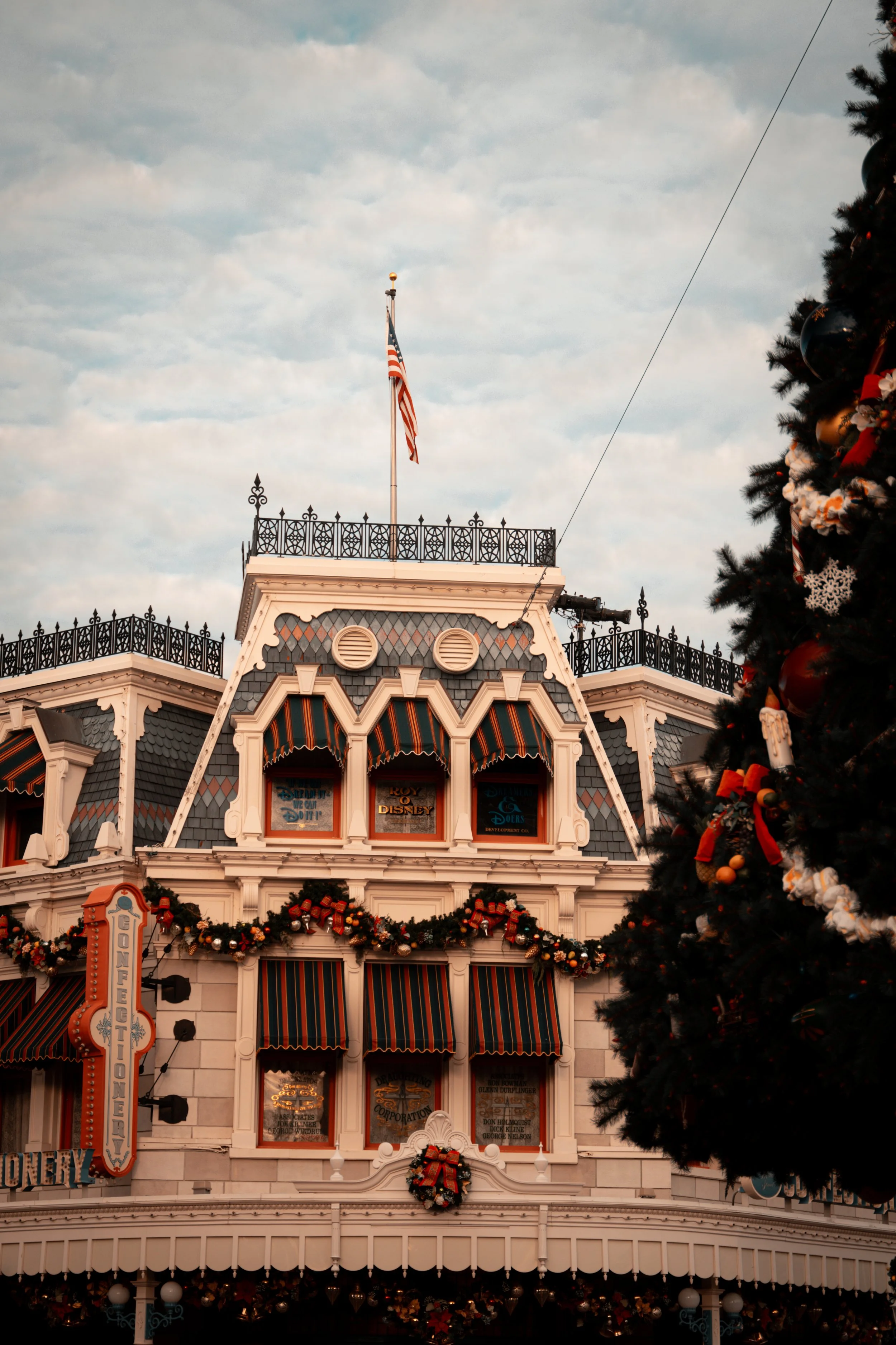 The Haunted Mansion building decorated for Christmas with garlands and wreaths, with an American flag on the roof, and a large Christmas tree on the right side.