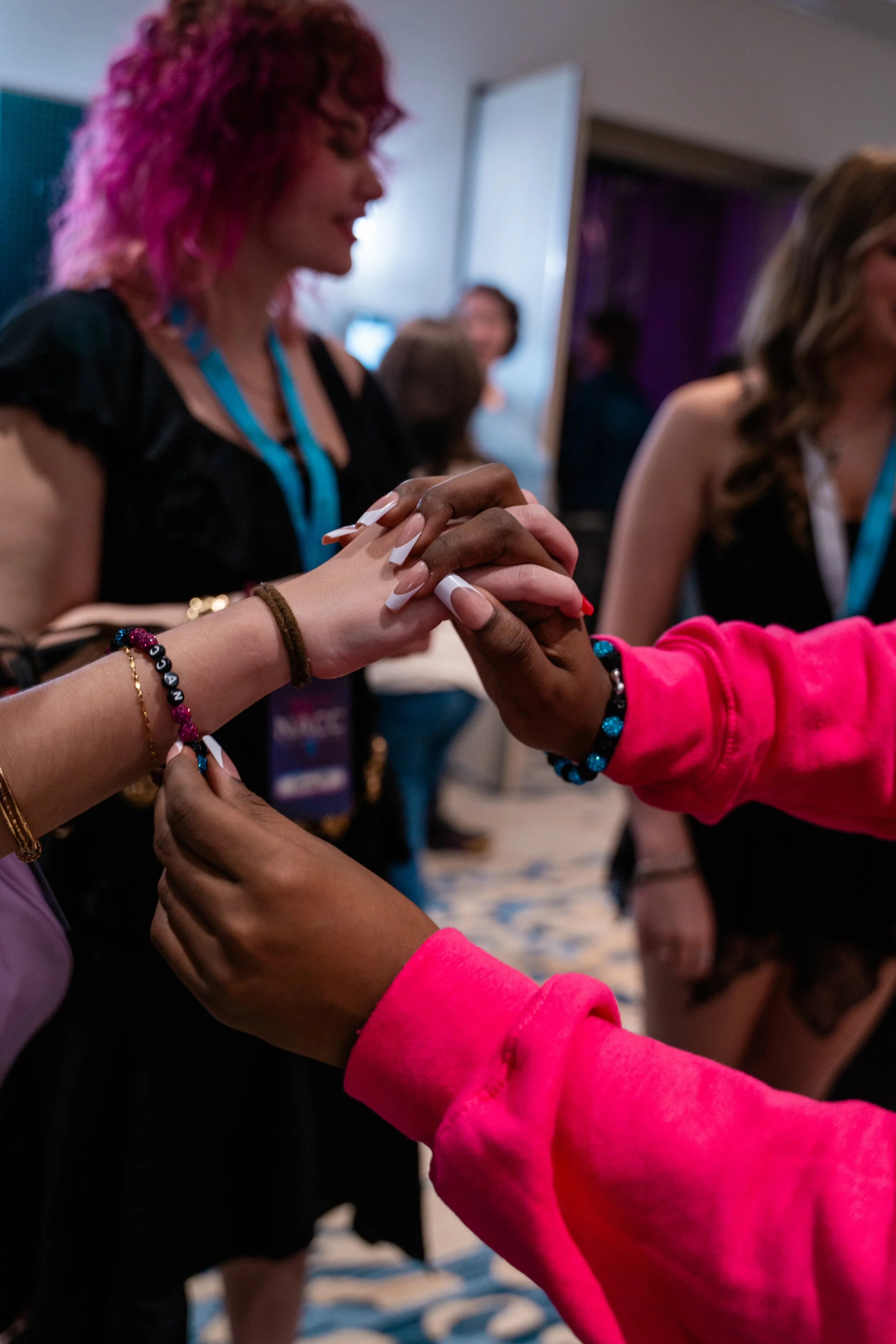 Two people holding hands, with one person's hand on top of the other's, in a close-up shot at an indoor event.