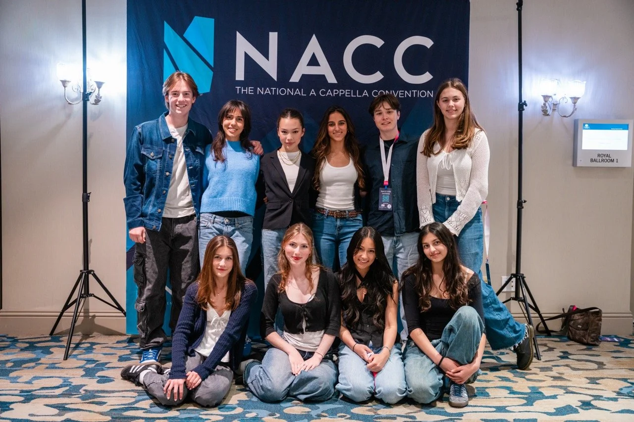 Group of eleven young people posing together at the NACC convention in front of a blue banner with the NACC logo, in a hotel conference room.