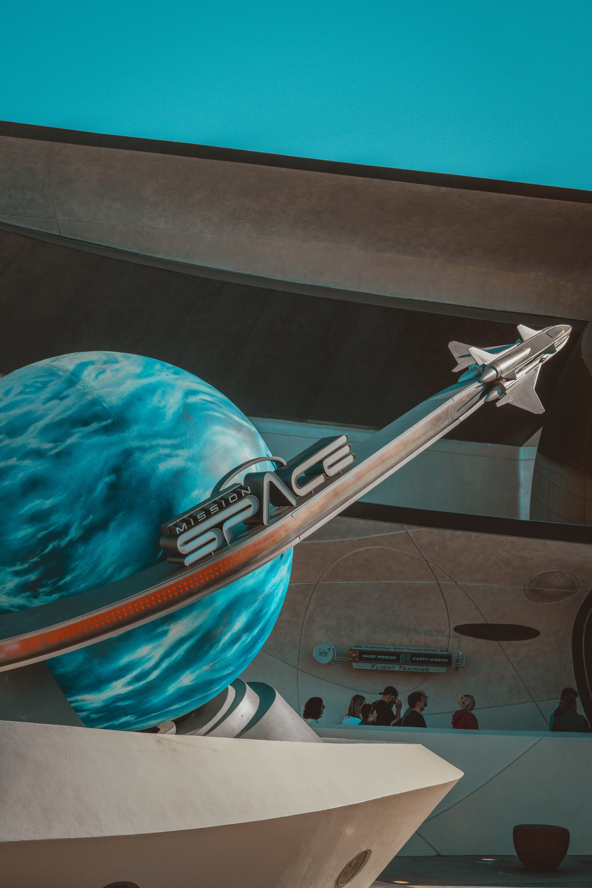 Interior space museum with a large globe and a model of a spacecraft labeled 'Mission Space', simulating a space launch with people observing.