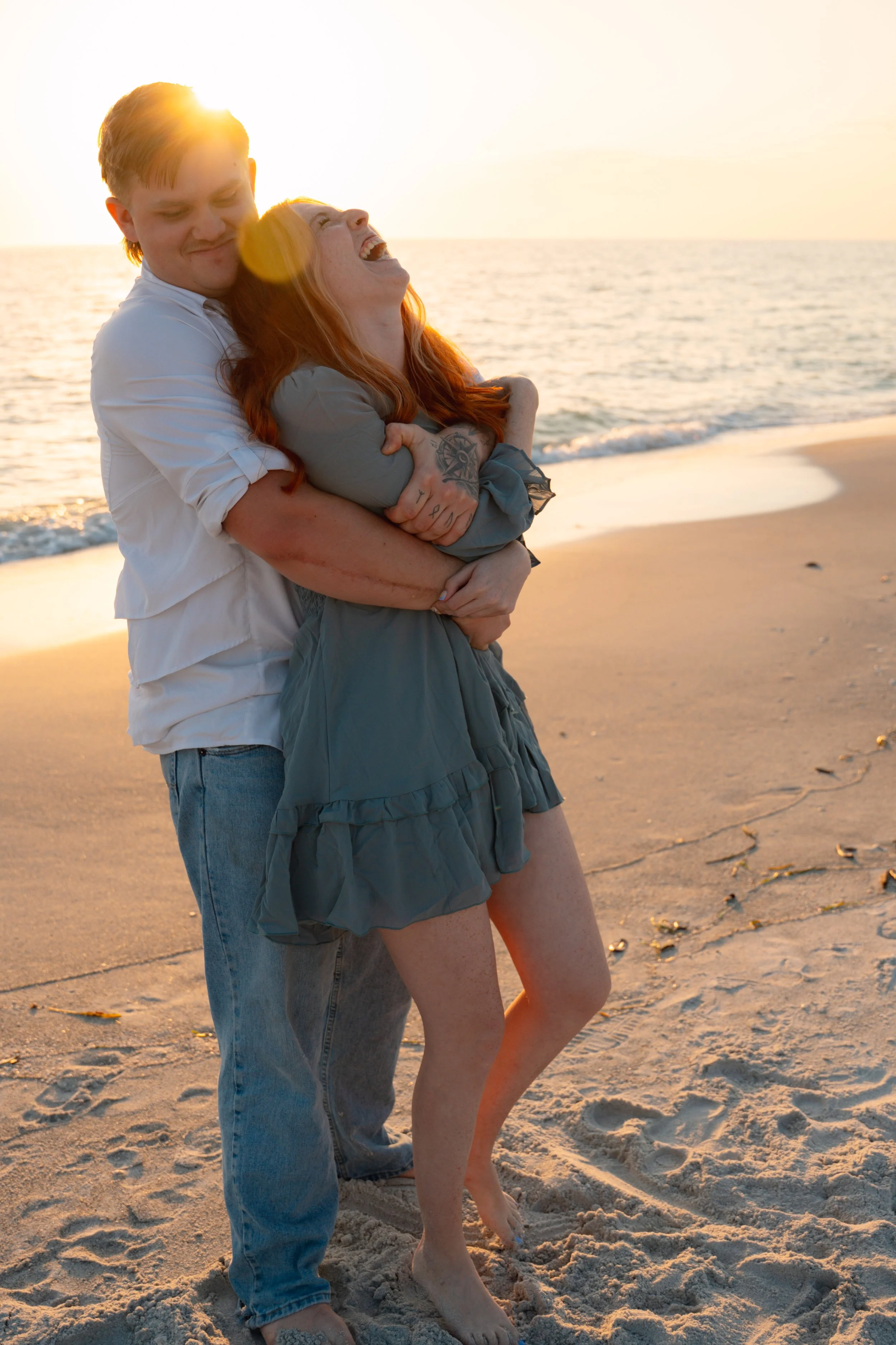 A couple hugging on the beach at sunset, smiling and enjoying each other's company.