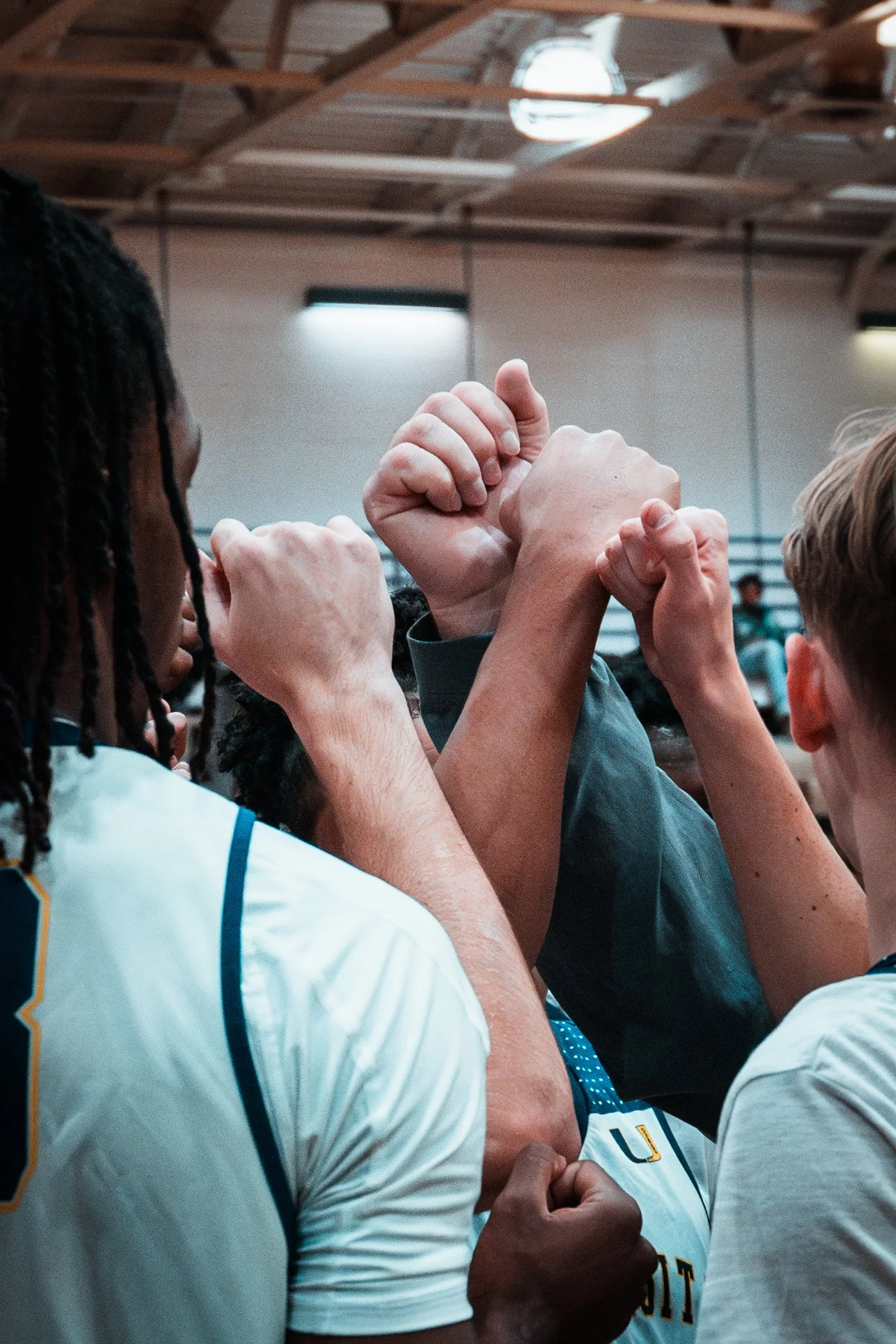 Group of athletes in a team huddle, raising their fists together in unity inside a gym.