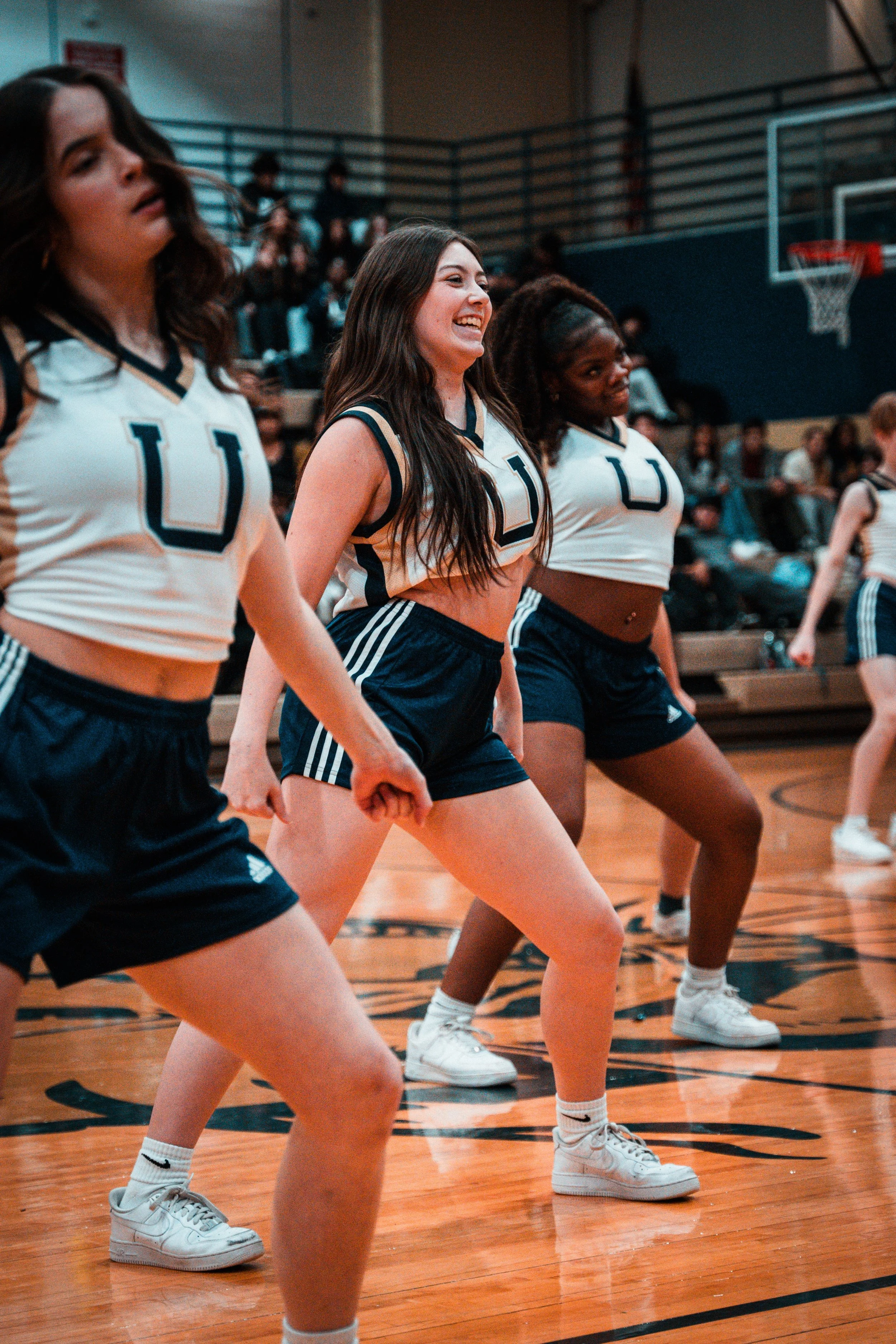 Women in cheerleading uniforms performing a routine on a basketball court during a game.