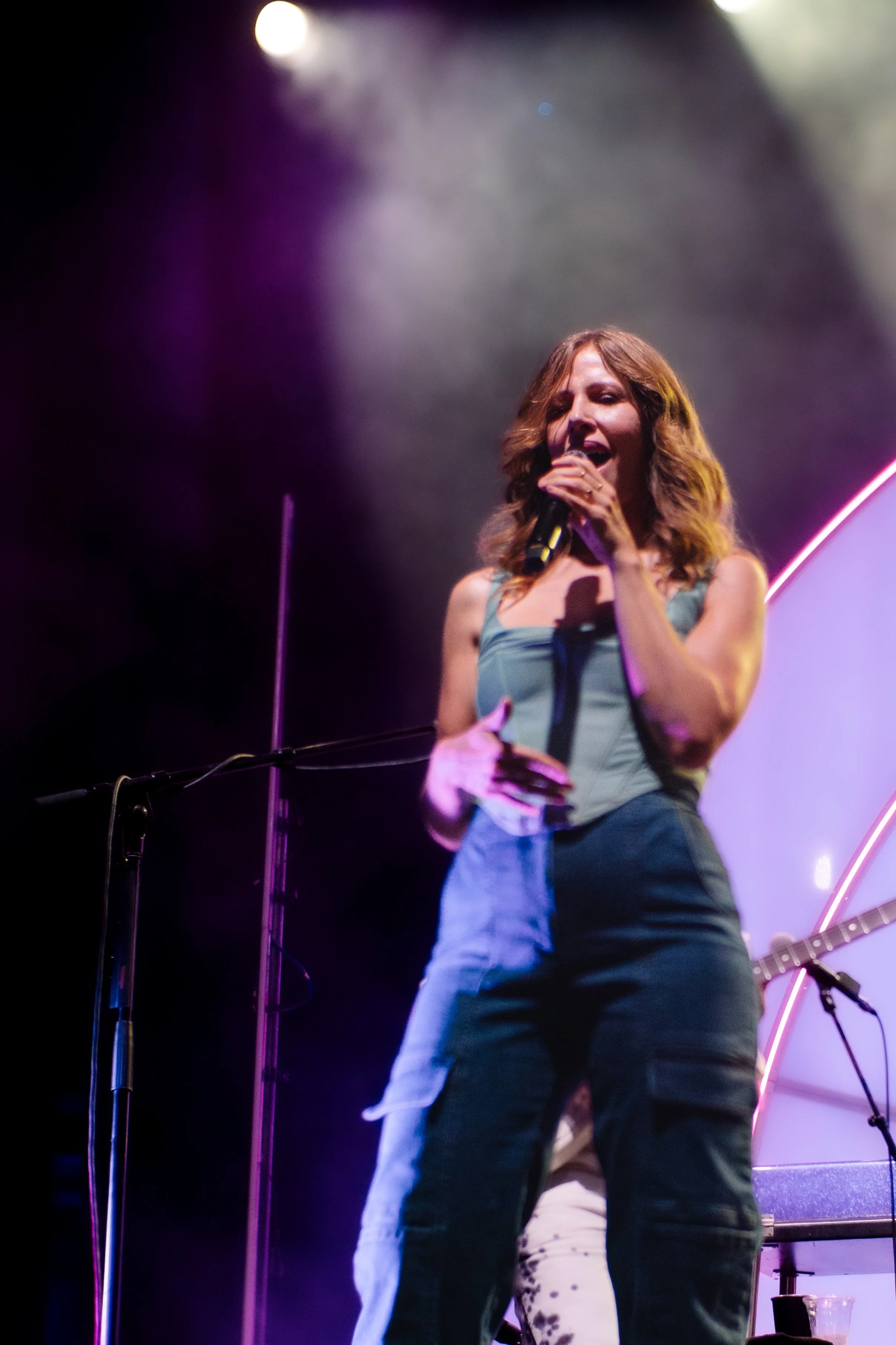 A woman singing into a microphone on stage with colorful lighting.