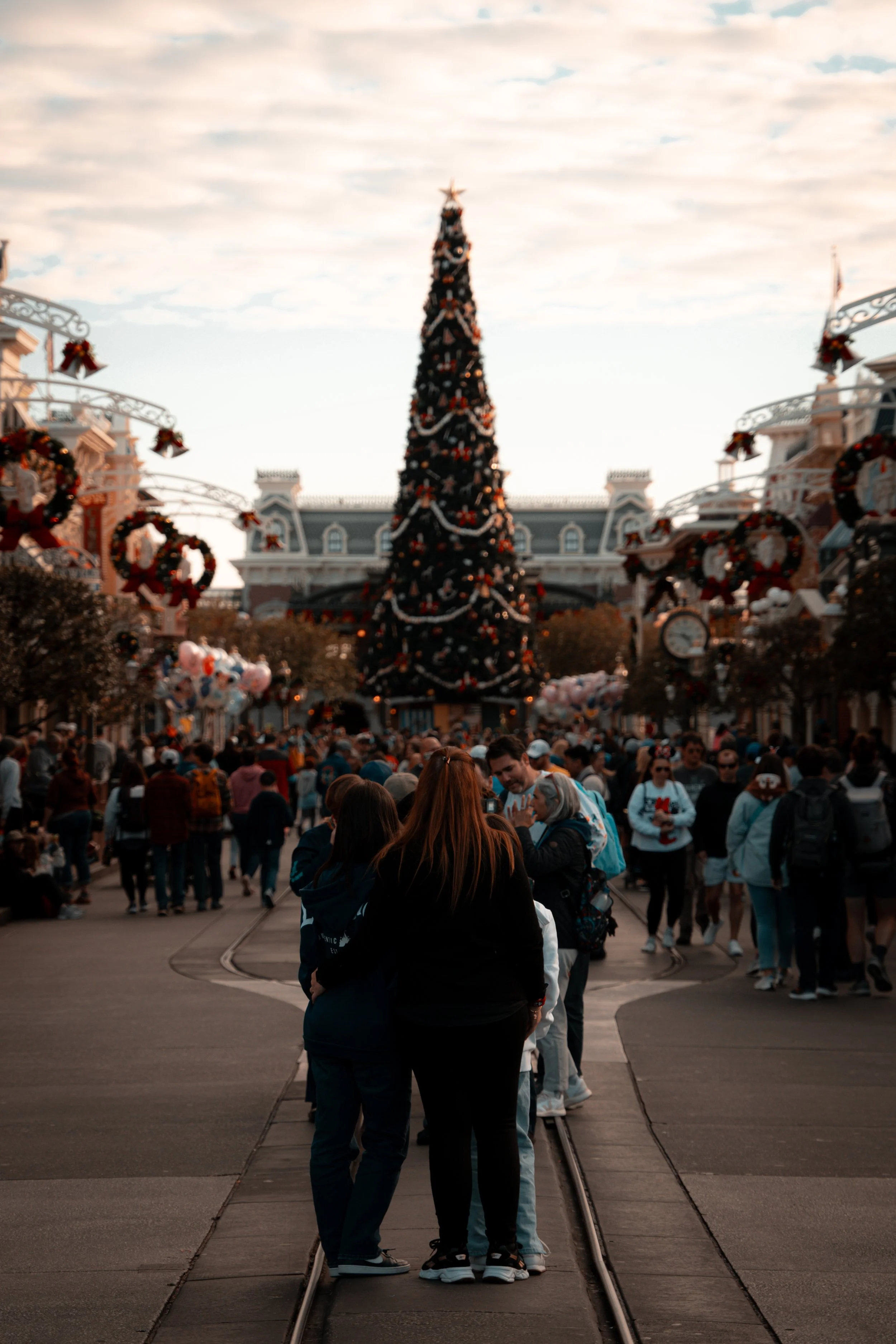 A large decorated Christmas tree with toys and lights at a theme park during the evening, with many visitors walking around.
