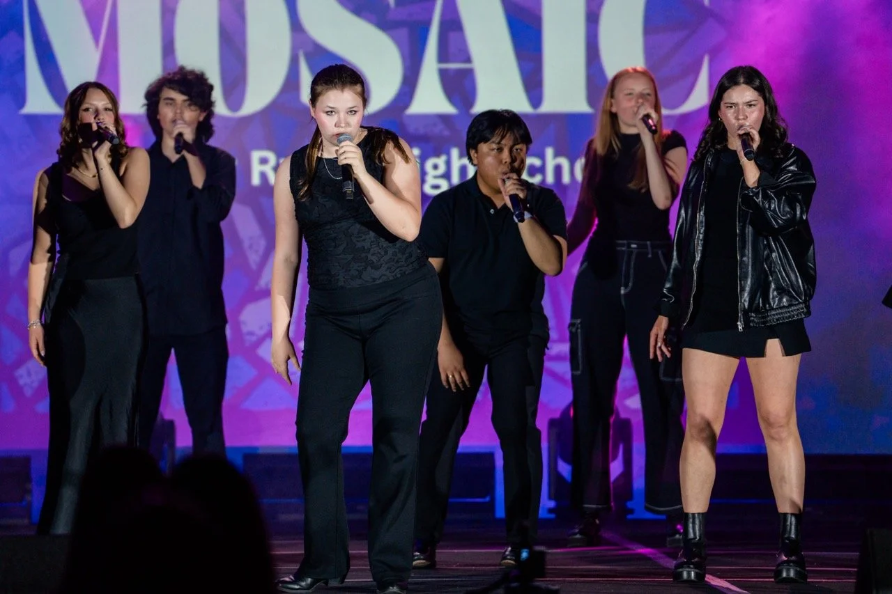 Six young performers with microphones on stage at a school musical.