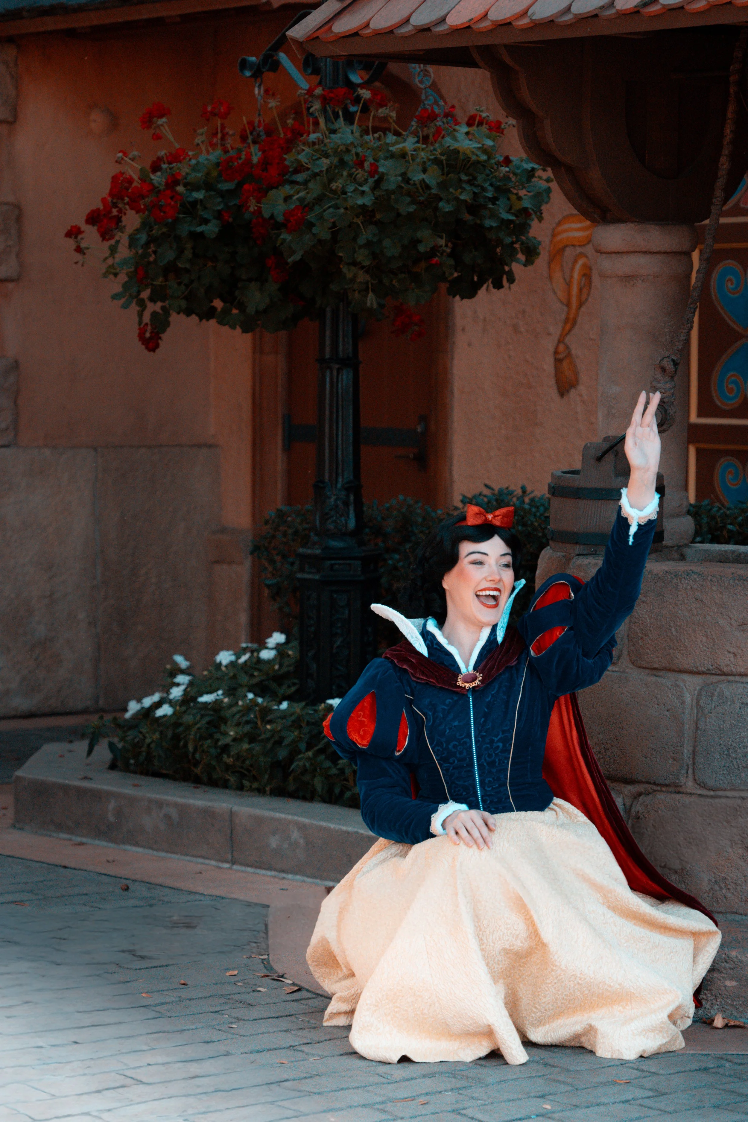 Woman dressed as Snow White sitting on a curb, smiling and waving.