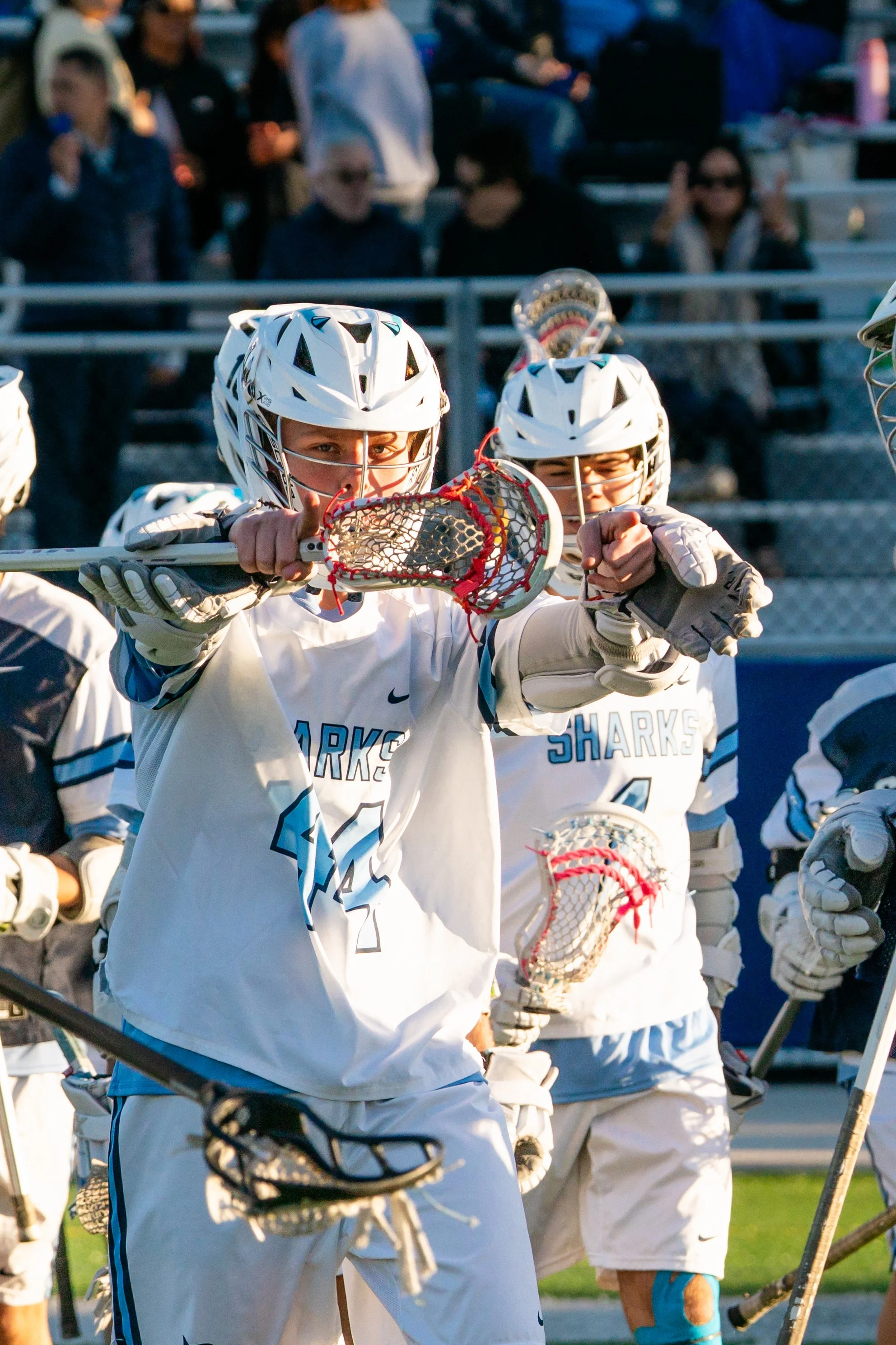 Lacrosse players in white uniforms and helmets on a sports field during a game.