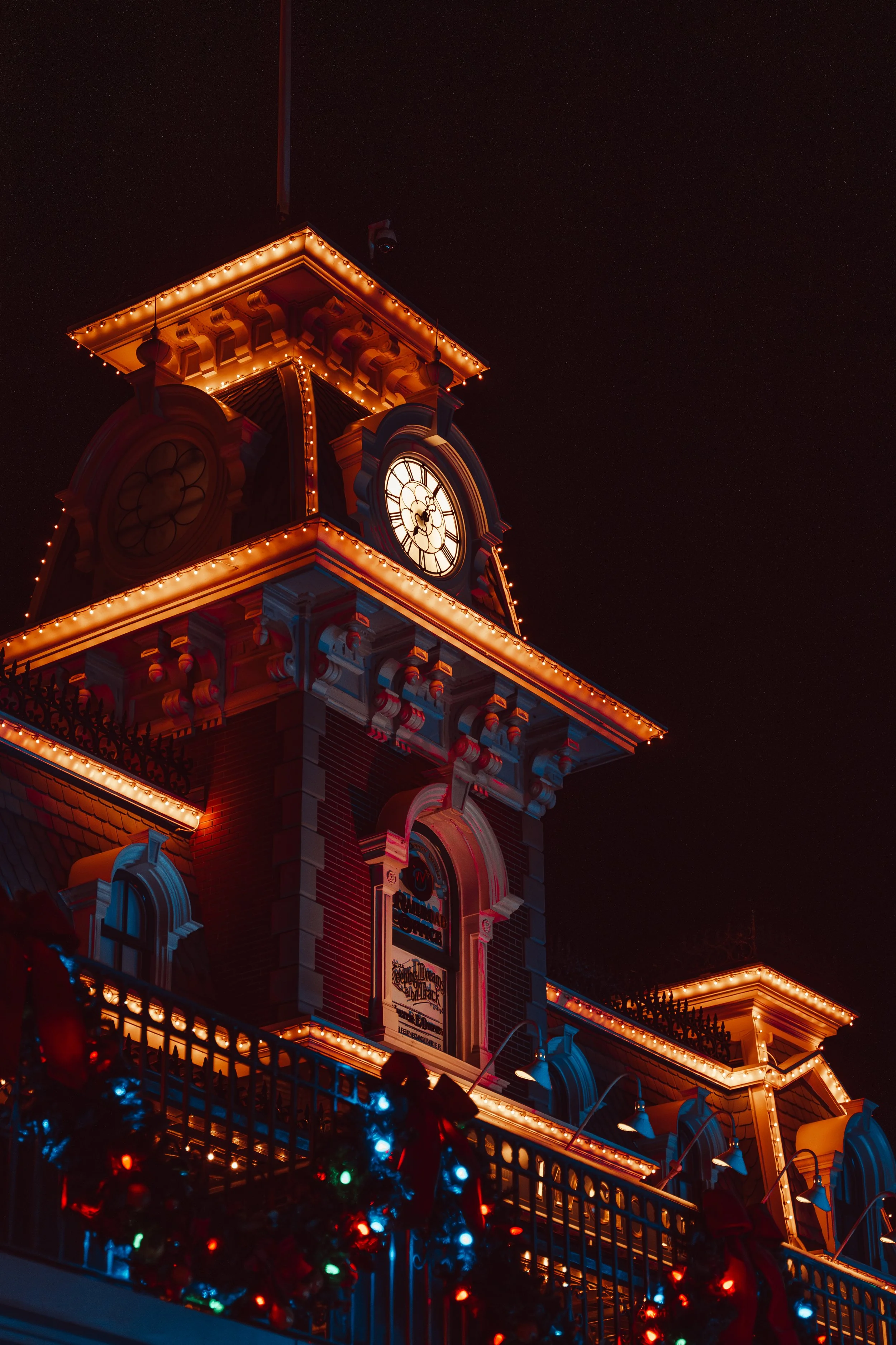 A city clock tower decorated with Christmas lights at night.
