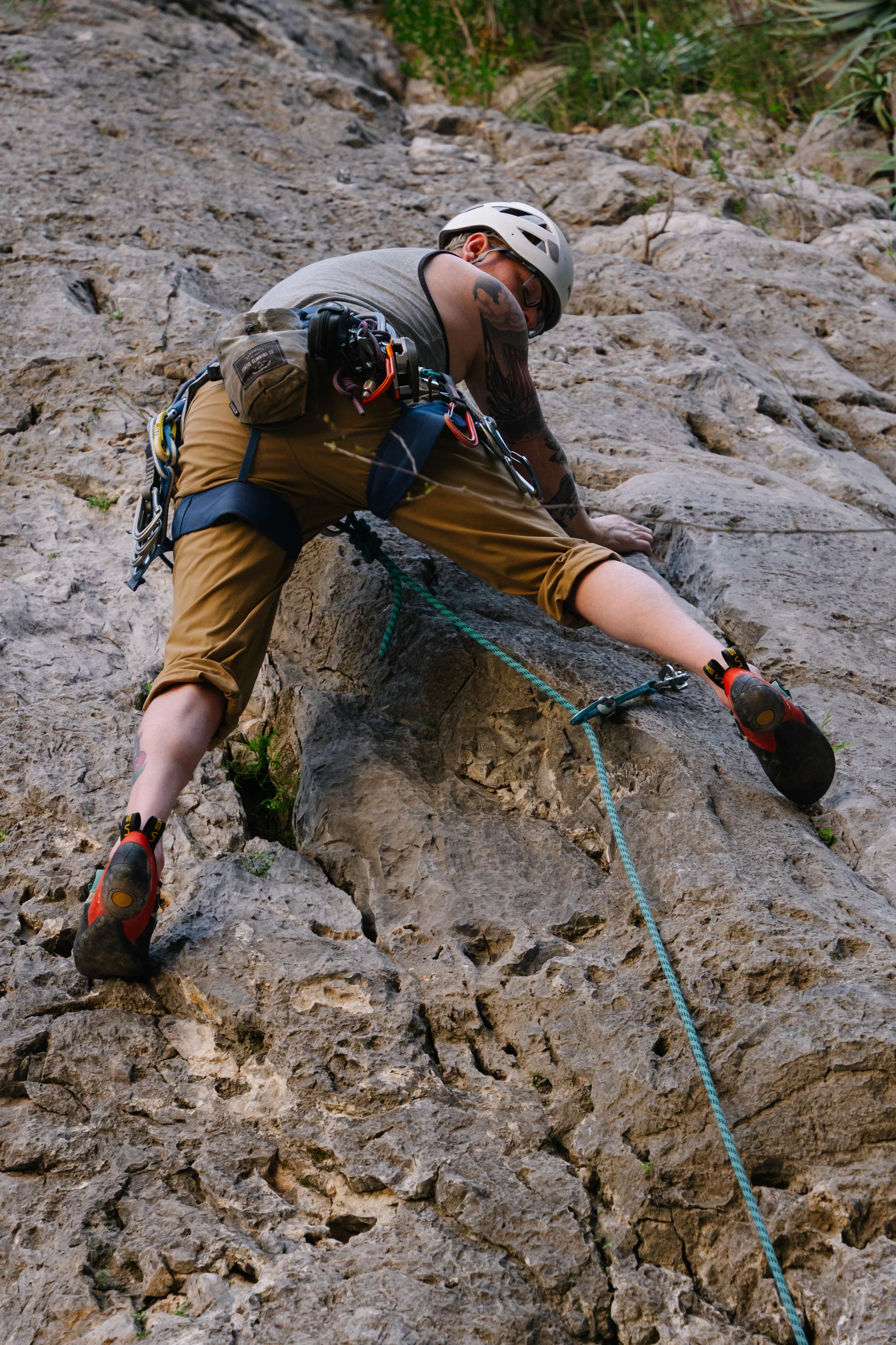 A man rock climbing on a steep outdoor rock face, wearing a helmet, climbing shoes, and harness, with a climbing rope attached.