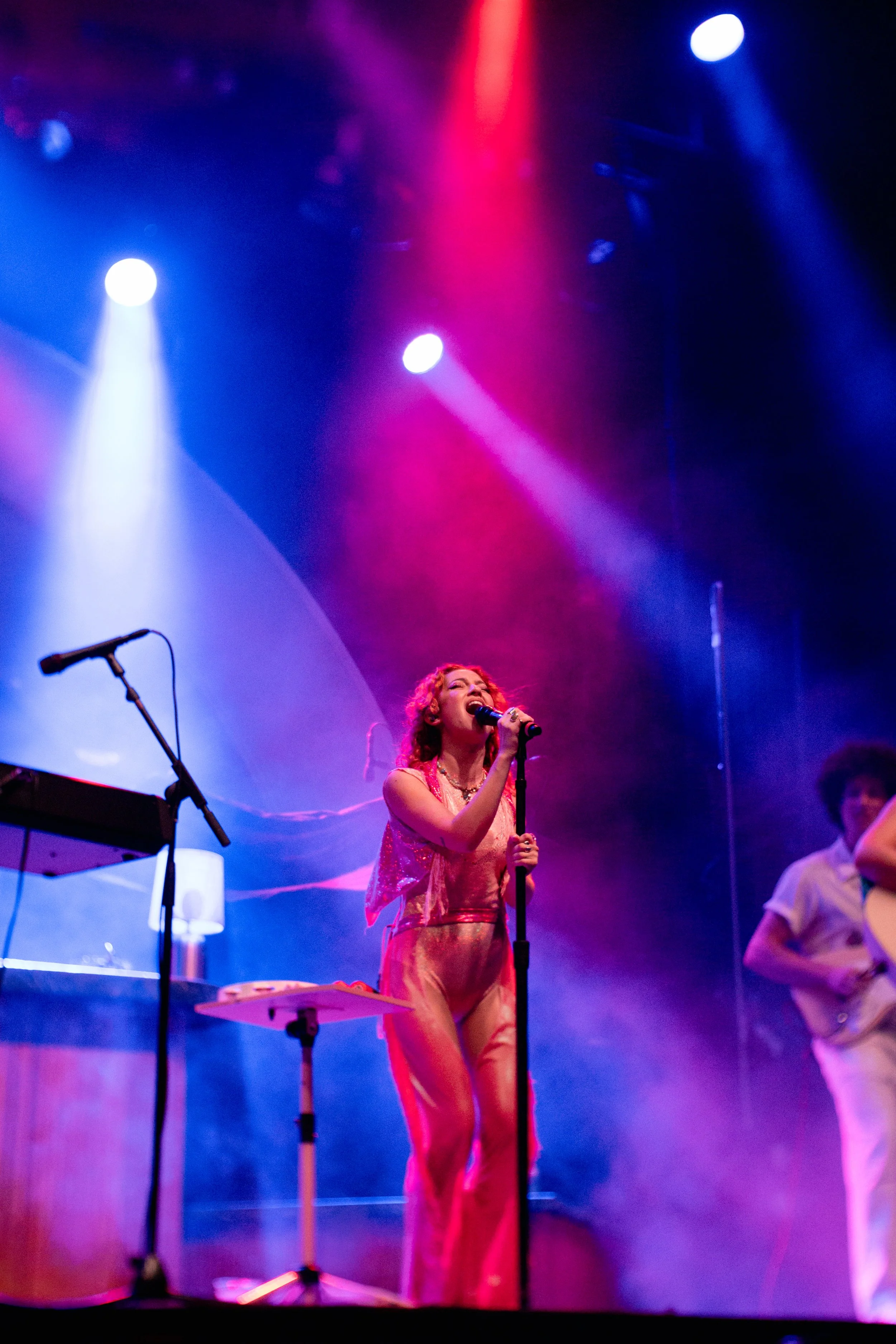 A woman singing on stage with colorful lighting, accompanied by musicians, in a concert setting.