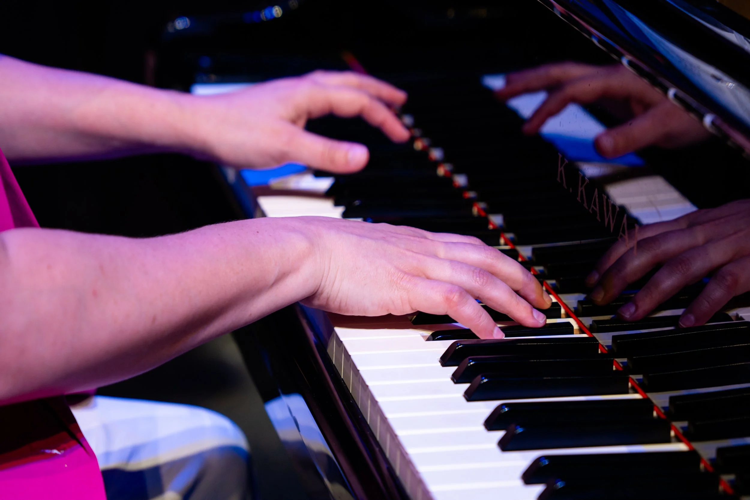 Close-up of two people playing a grand piano, focusing on their hands on the keyboard.