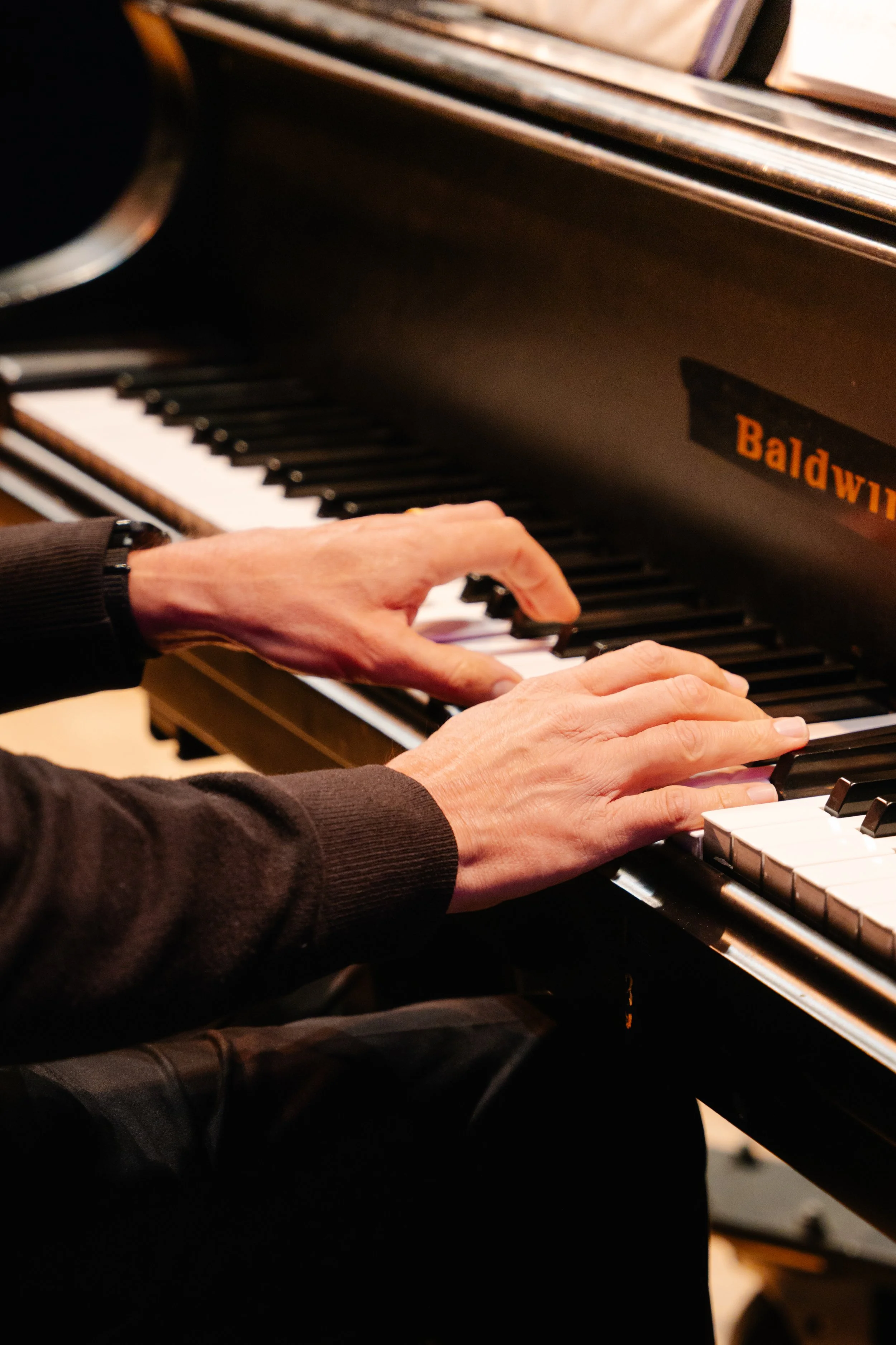 Close-up of a person playing a Baldwin piano, with visible hands on the keyboard.