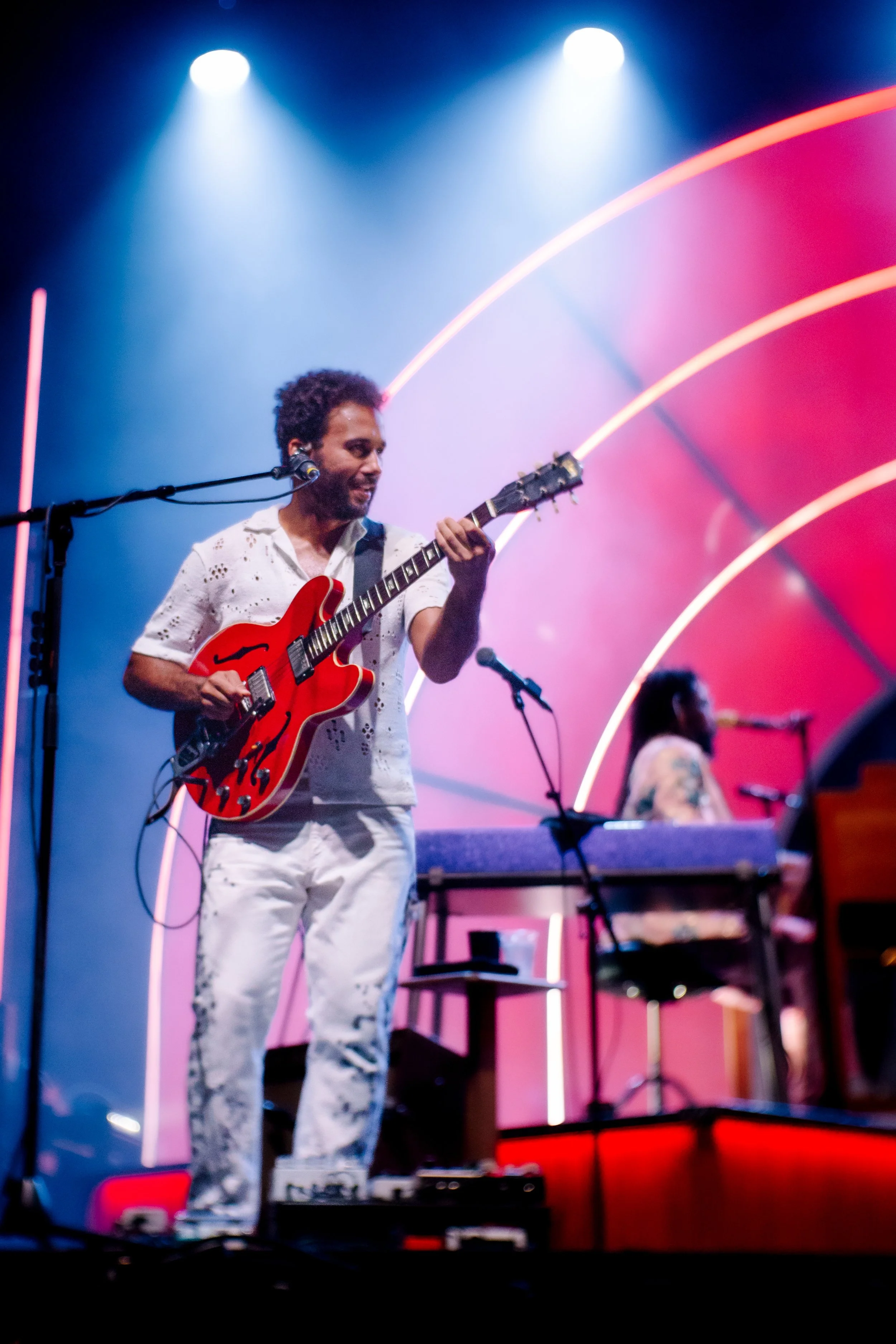 Musician playing red electric guitar on stage with blue and pink neon lights.