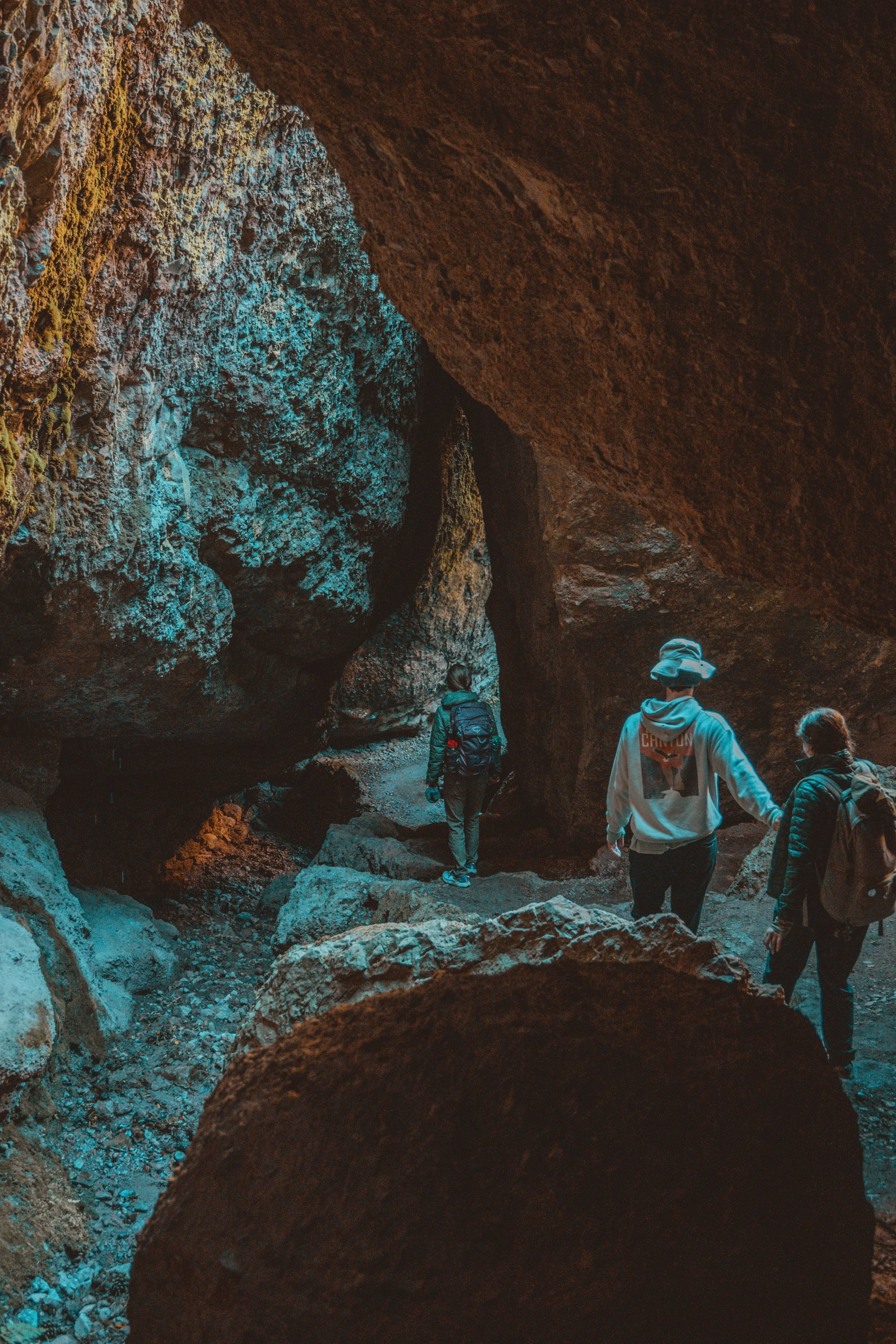 Three people exploring a dark, rocky cave, walking on uneven terrain.