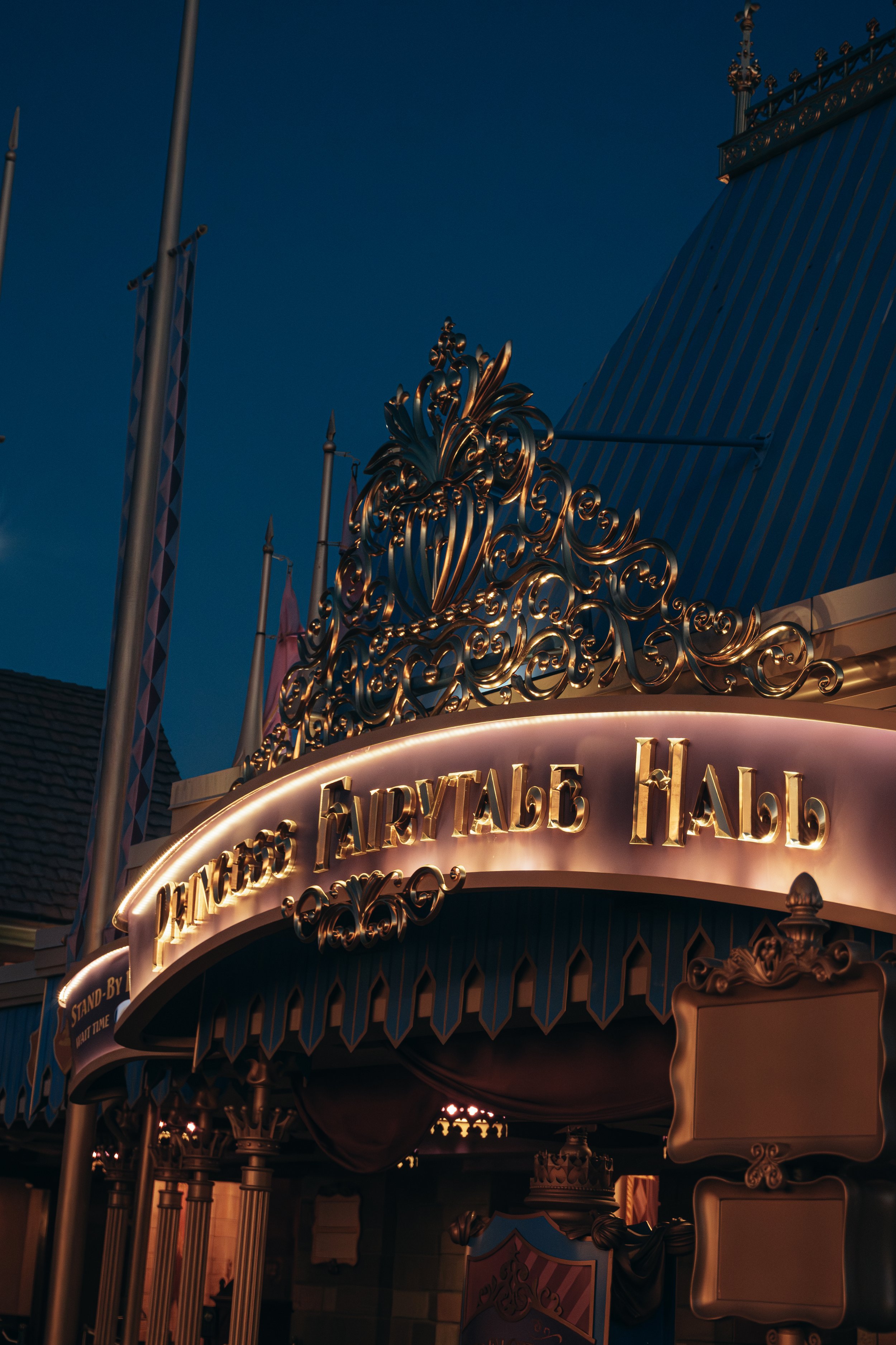 Entrance to a fairy tale land theme park with ornate gold decorations and a sign in Russian that says "In the Fairy Tale Land" during evening hours.