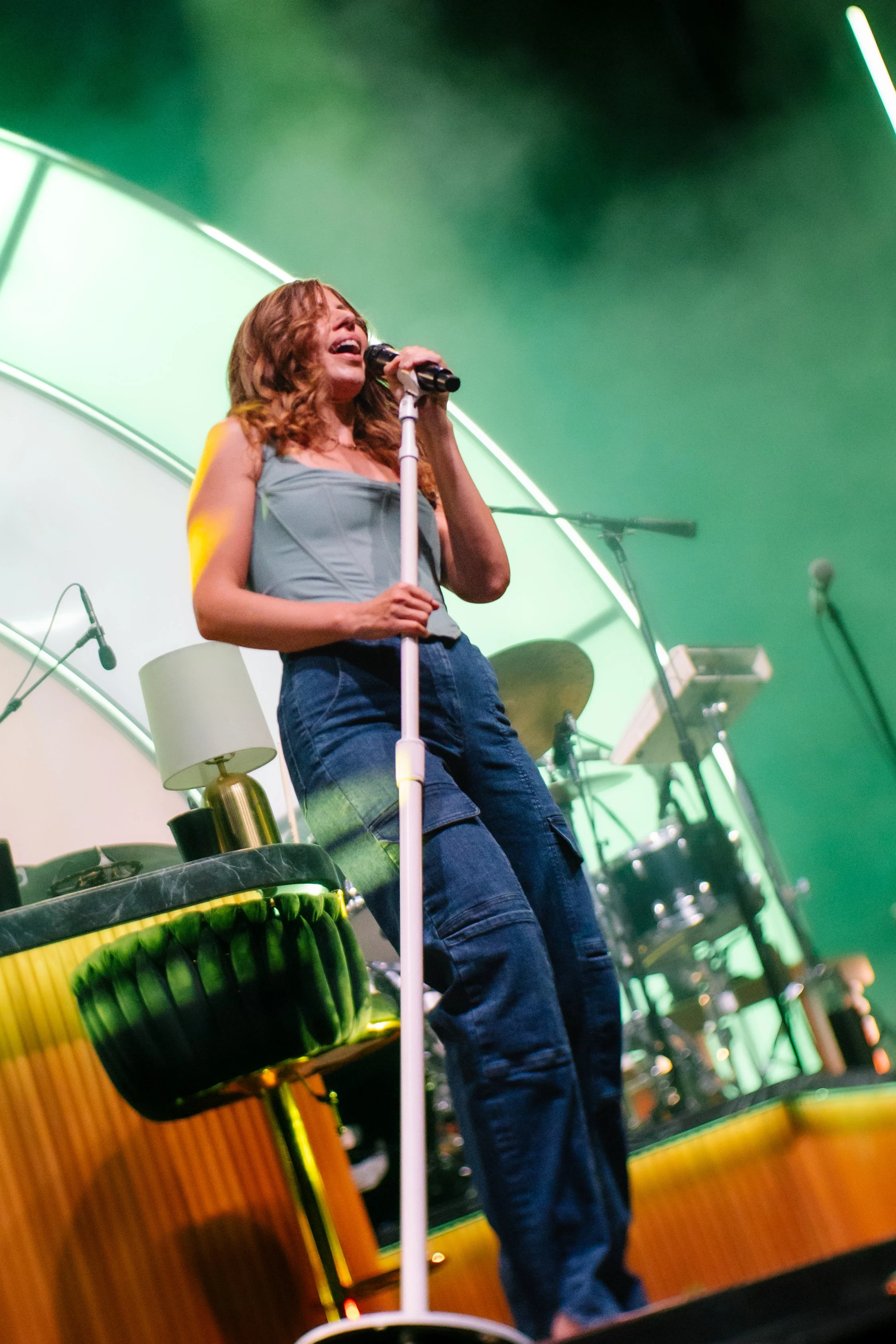 A woman singing on stage with musical instruments and green and yellow stage lighting.