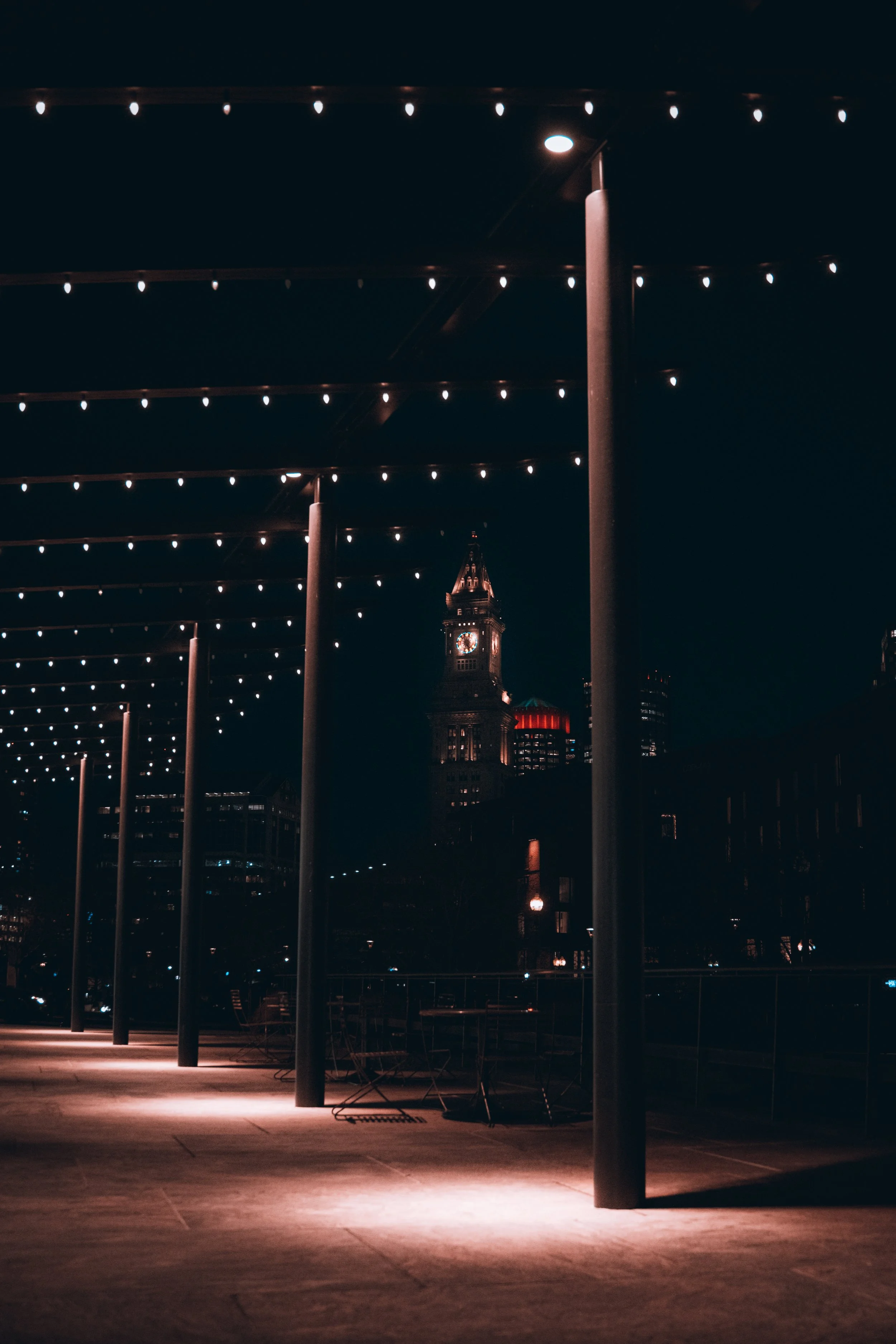 Nighttime city scene with string lights overhead and a historic clock tower illuminated in the background.