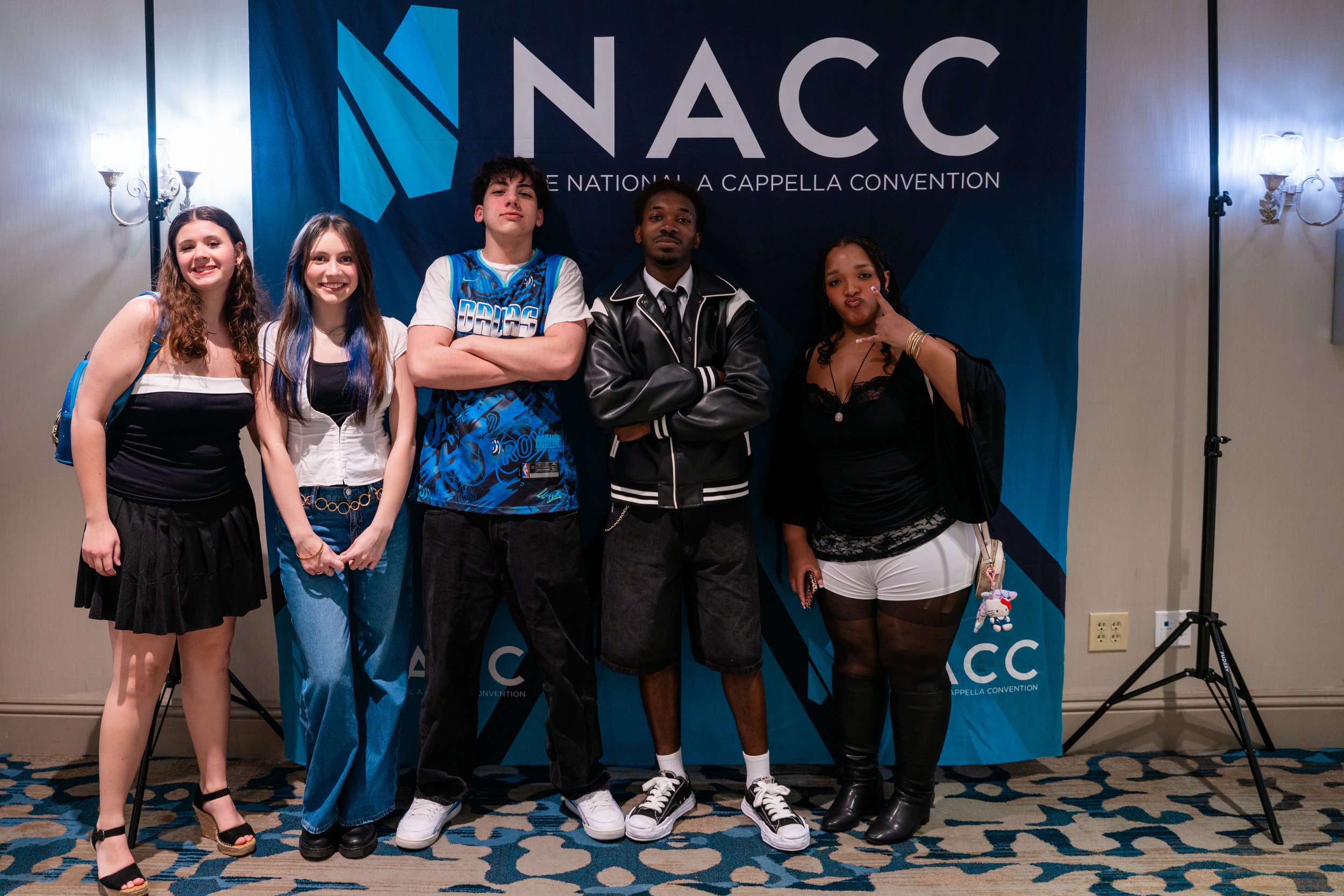 Five young people standing in front of a blue NACCC banner at a convention, posing for a group photo indoors.