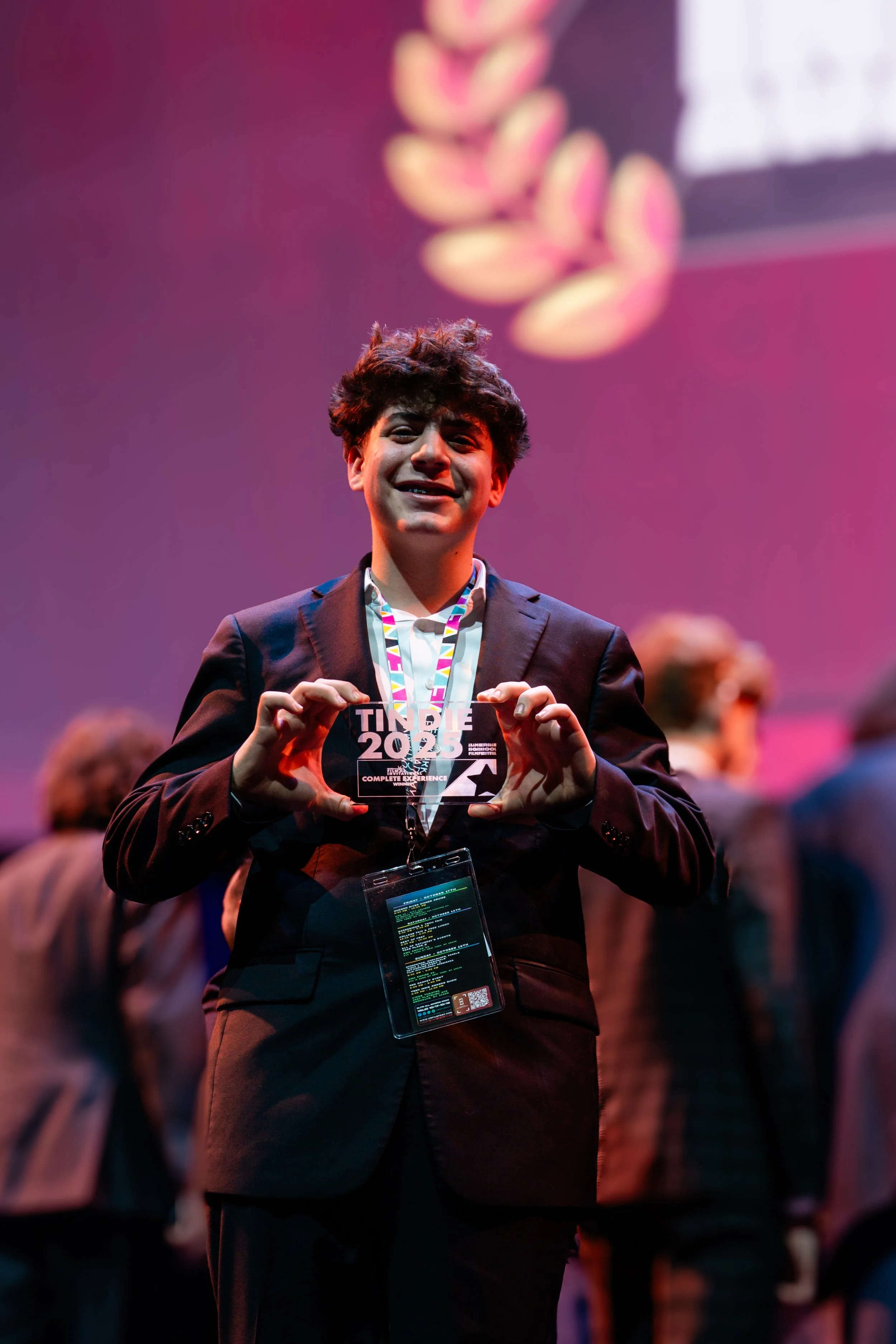 A young man in a suit smiling and holding a clear plaque with the text 'TIME 2023' at an indoor event.