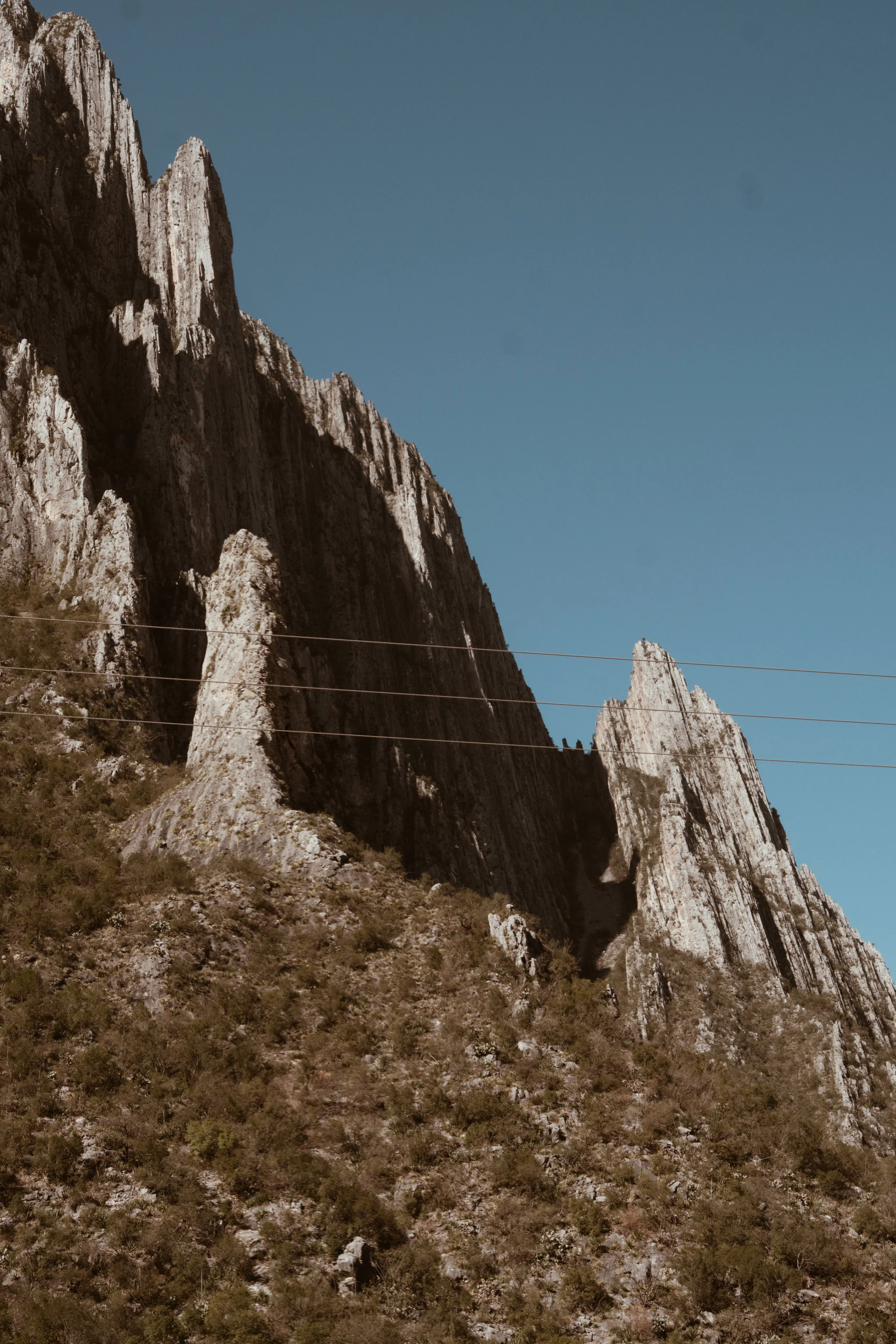 Tall rocky mountain with steep cliffs and sparse vegetation on the slope, under a clear blue sky.