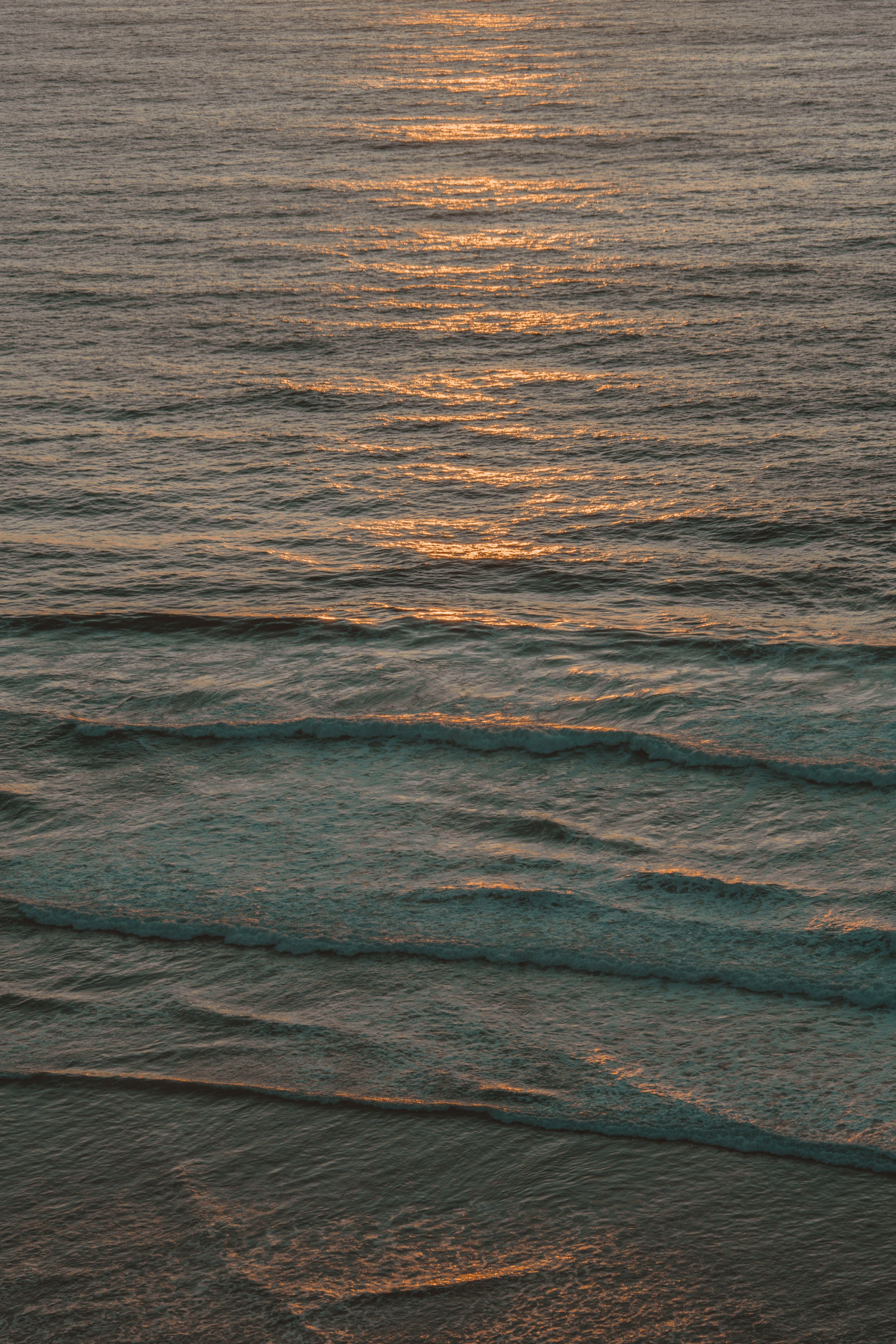 Sunset over the ocean with gentle waves reflecting the sunlight.