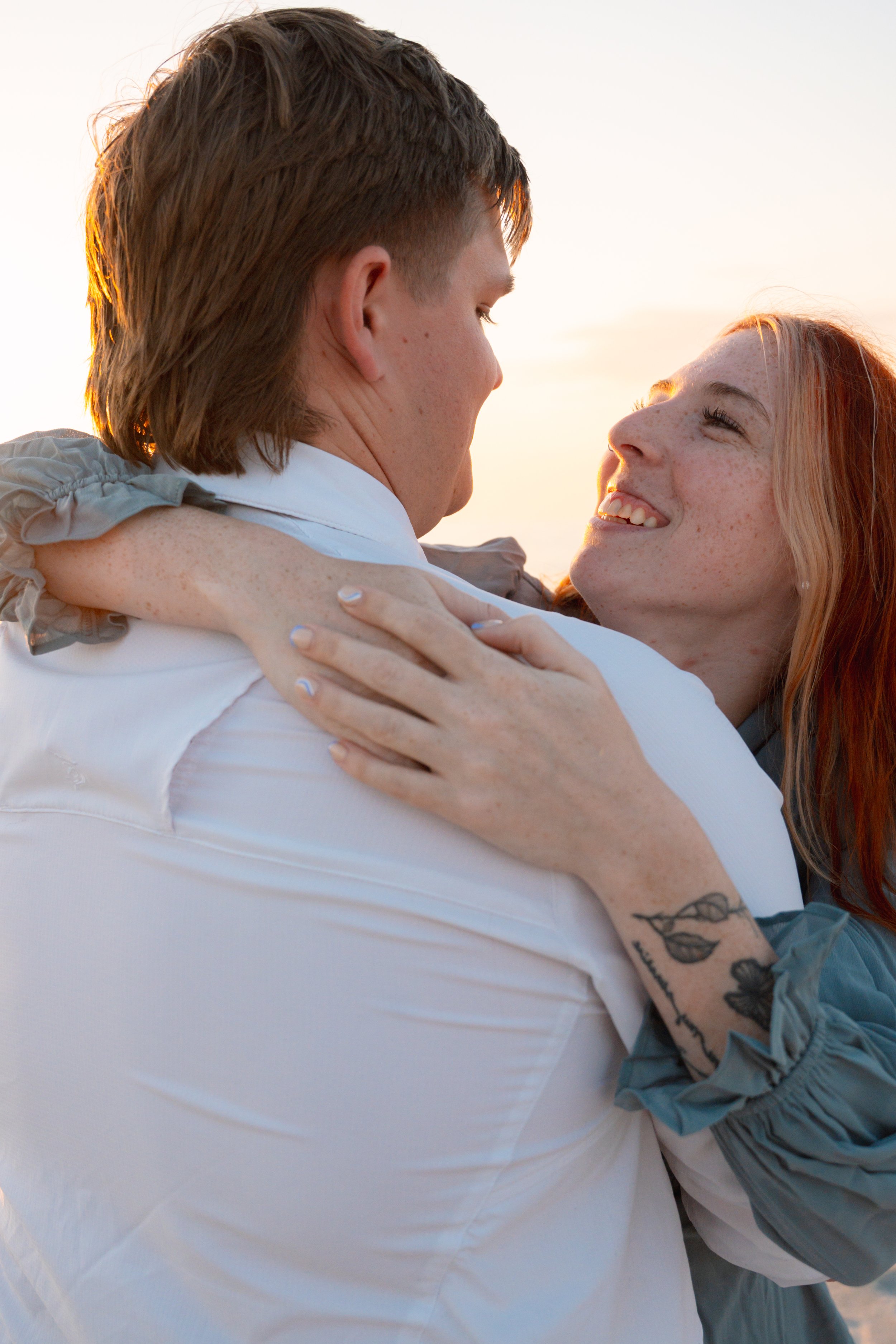 Couple embracing outdoors during sunset, smiling and looking into each other's eyes.