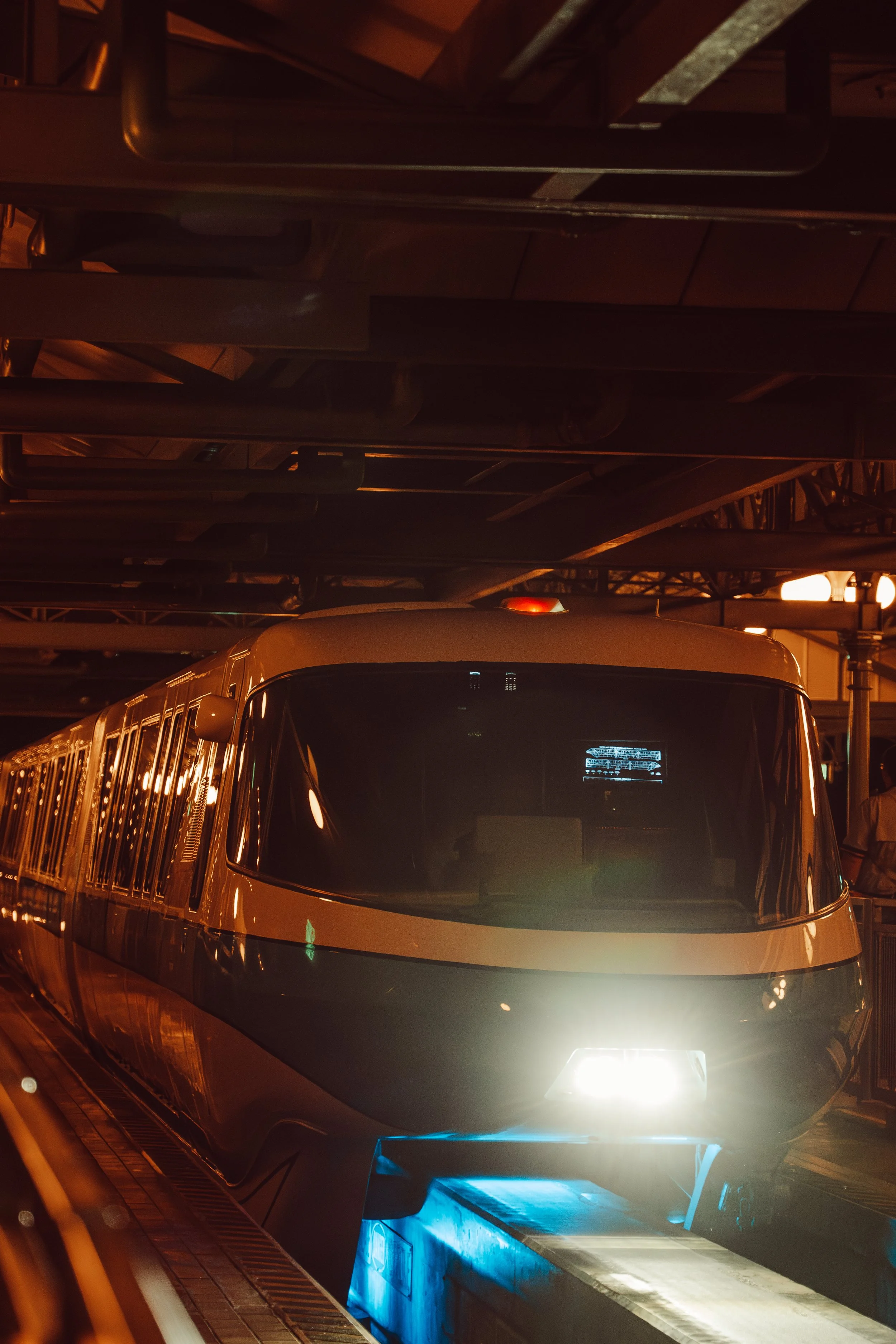 A futuristic train with a sleek design and bright headlight on a track at night, illuminated with blue and white lights.