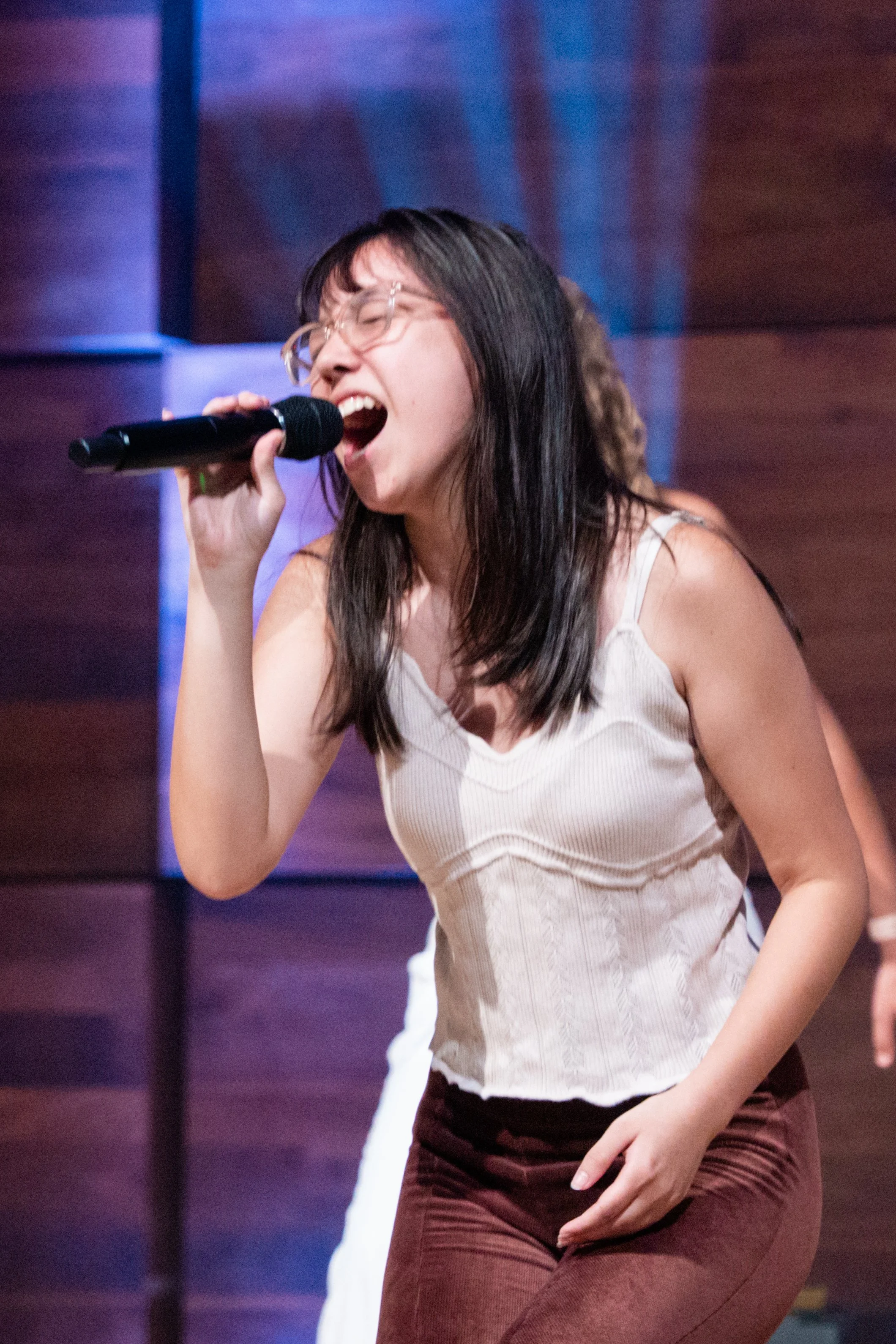 A woman singing passionately into a microphone on stage with a wooden background.
