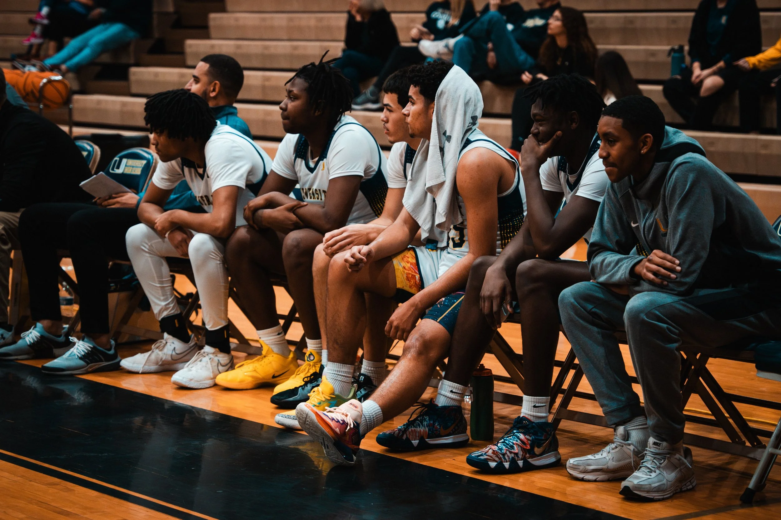 Basketball players sitting on benches during a game or practice in an indoor gym.