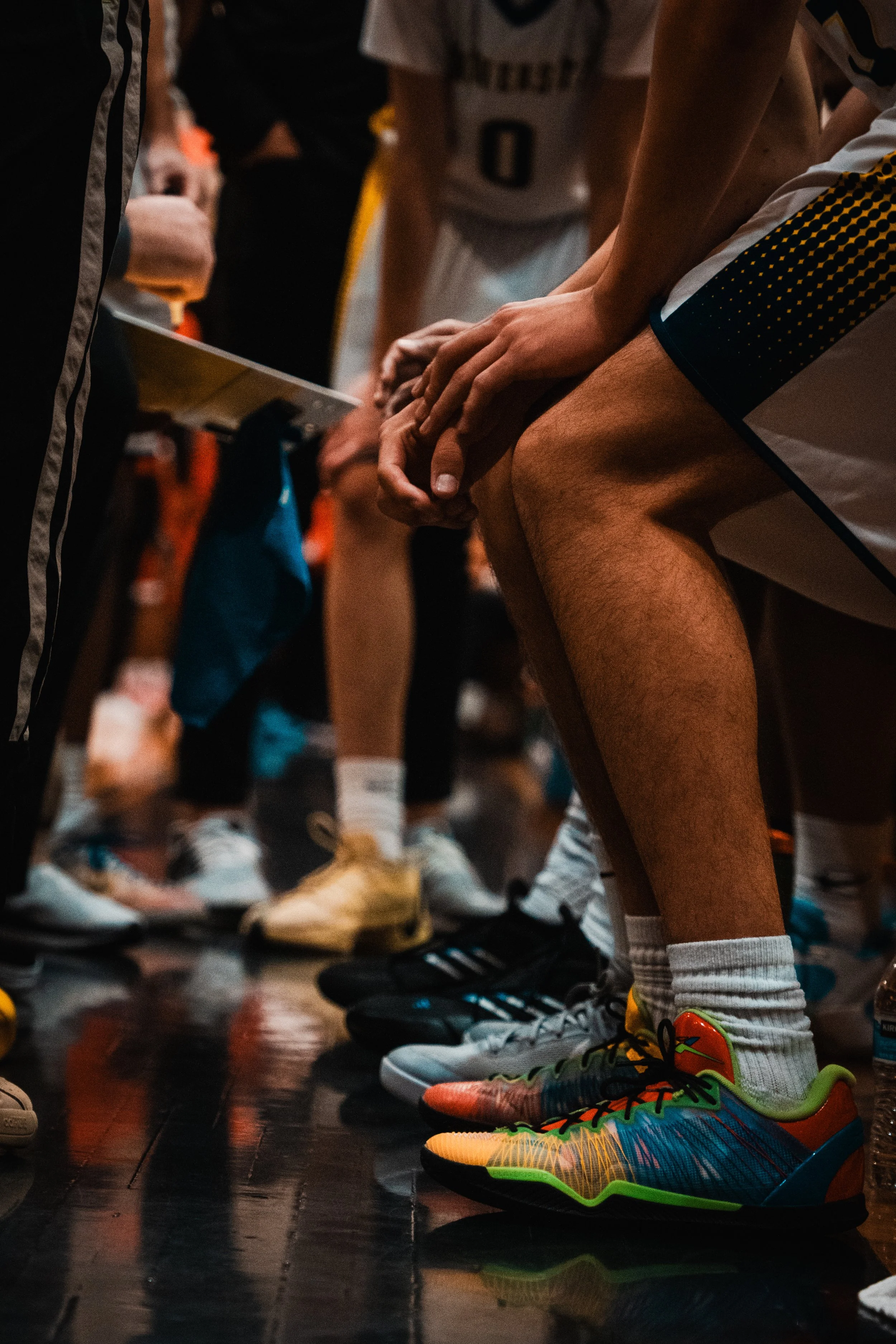 Basketball players huddled during a timeout, focusing on their colorful athletic shoes and hands in the center.