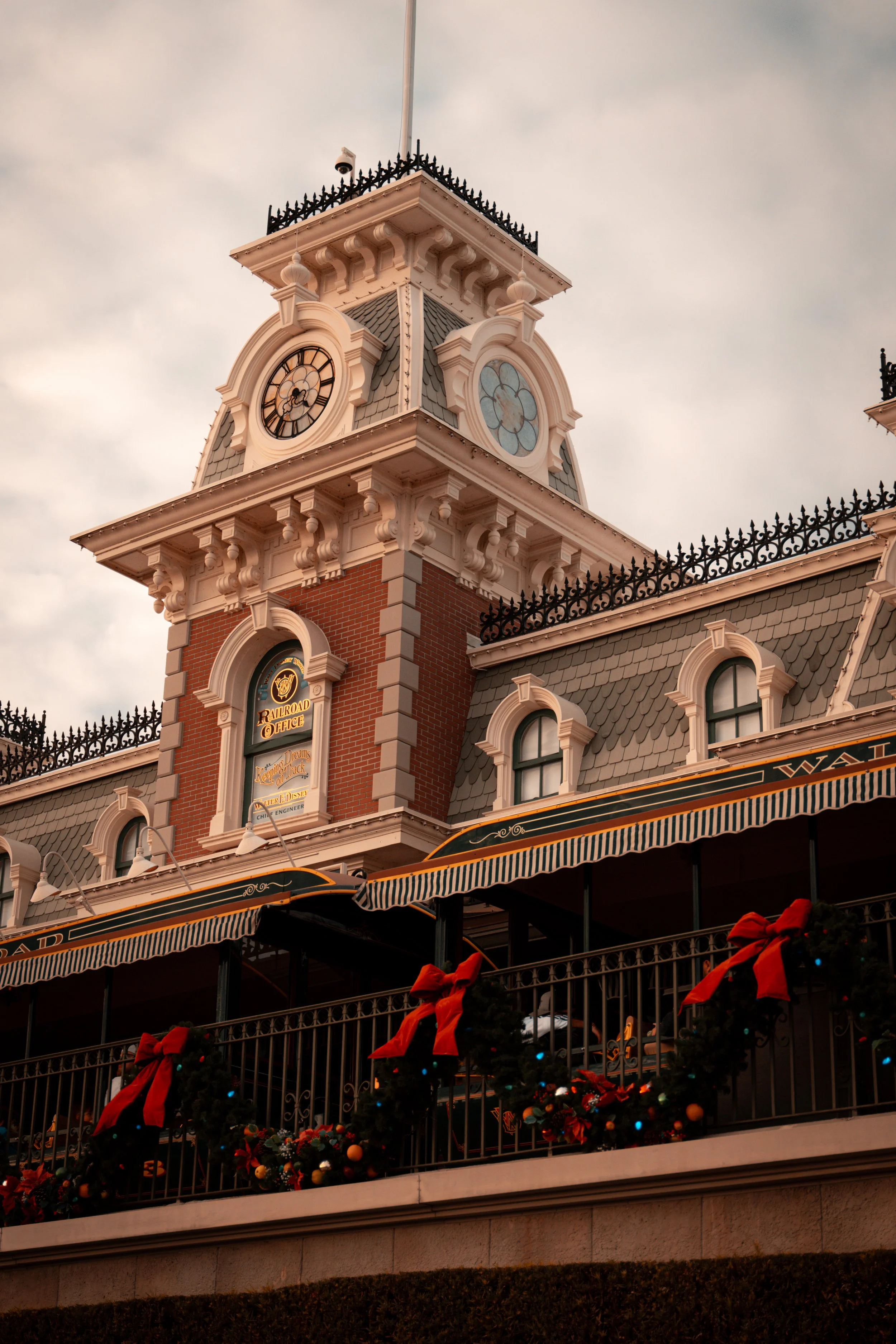 A Victorian-style building with a large clock tower, decorated for Christmas with wreaths and red bows on the railing.