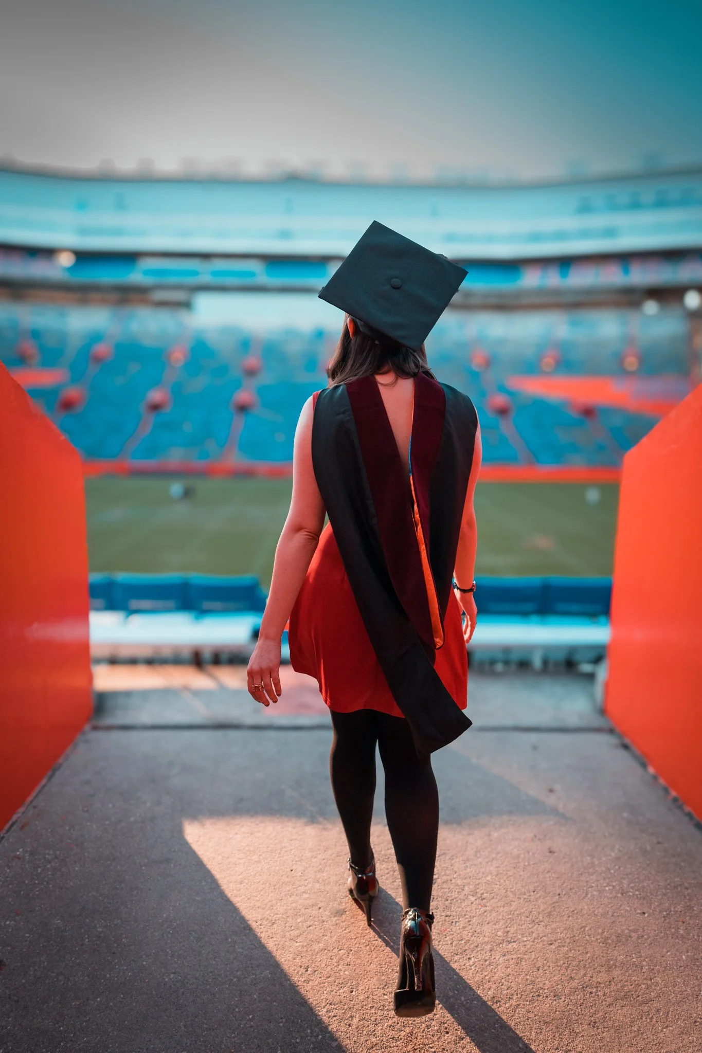 A woman in a graduation cap and gown walking through a stadium entrance.