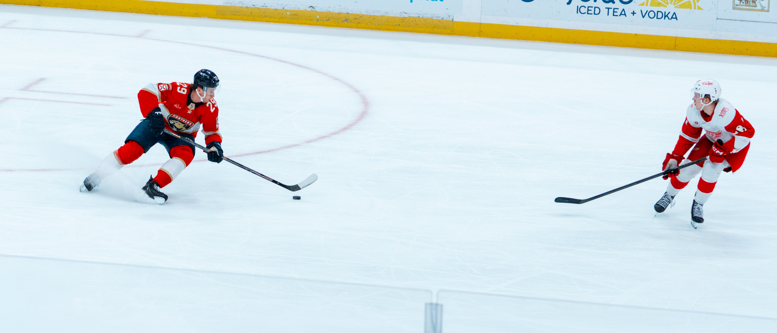 Two ice hockey players, one in a red and black uniform and the other in a white and red uniform, compete for the puck on the ice rink.