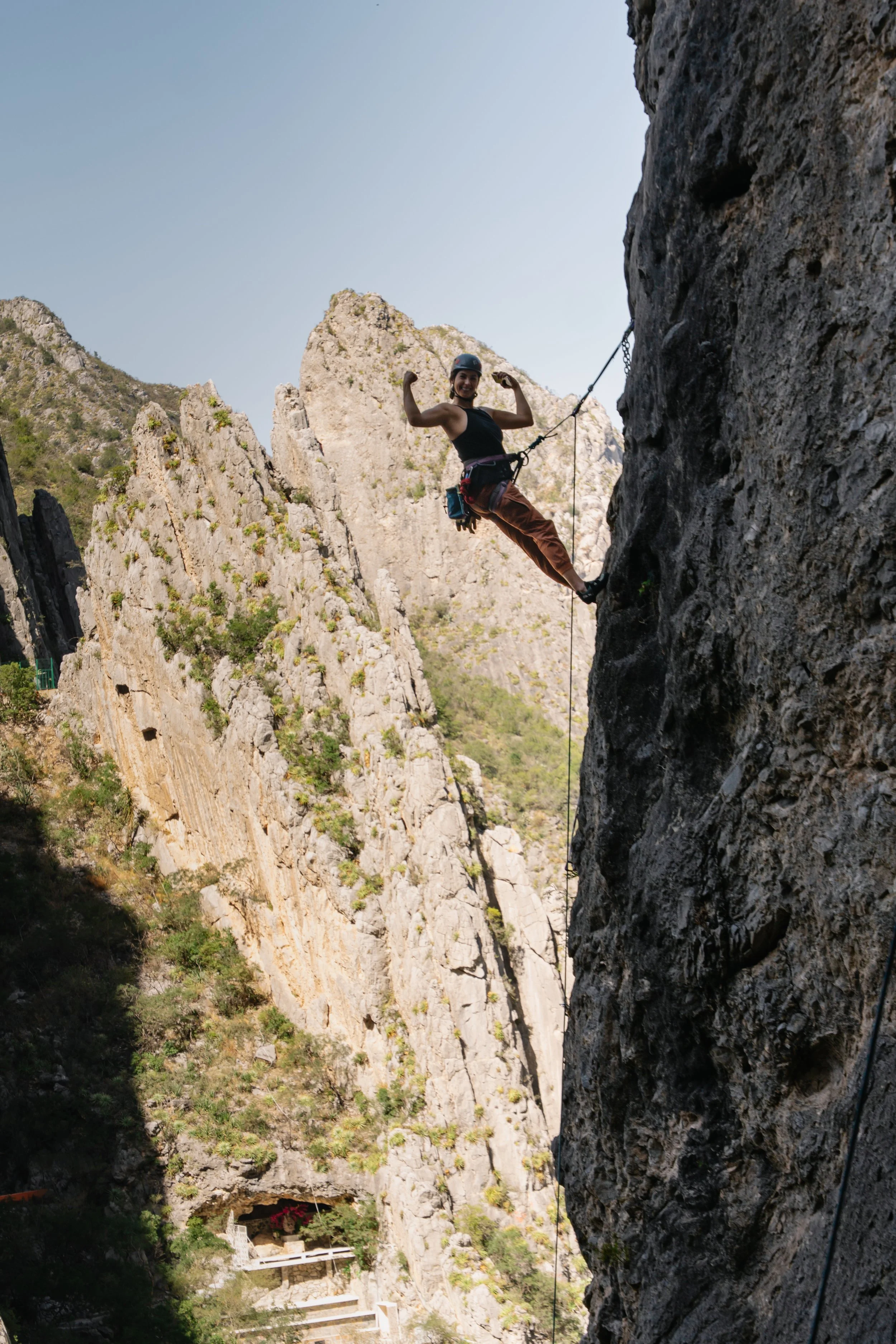 A woman climbing a steep rock face using safety gear and a harness, with mountains in the background.
