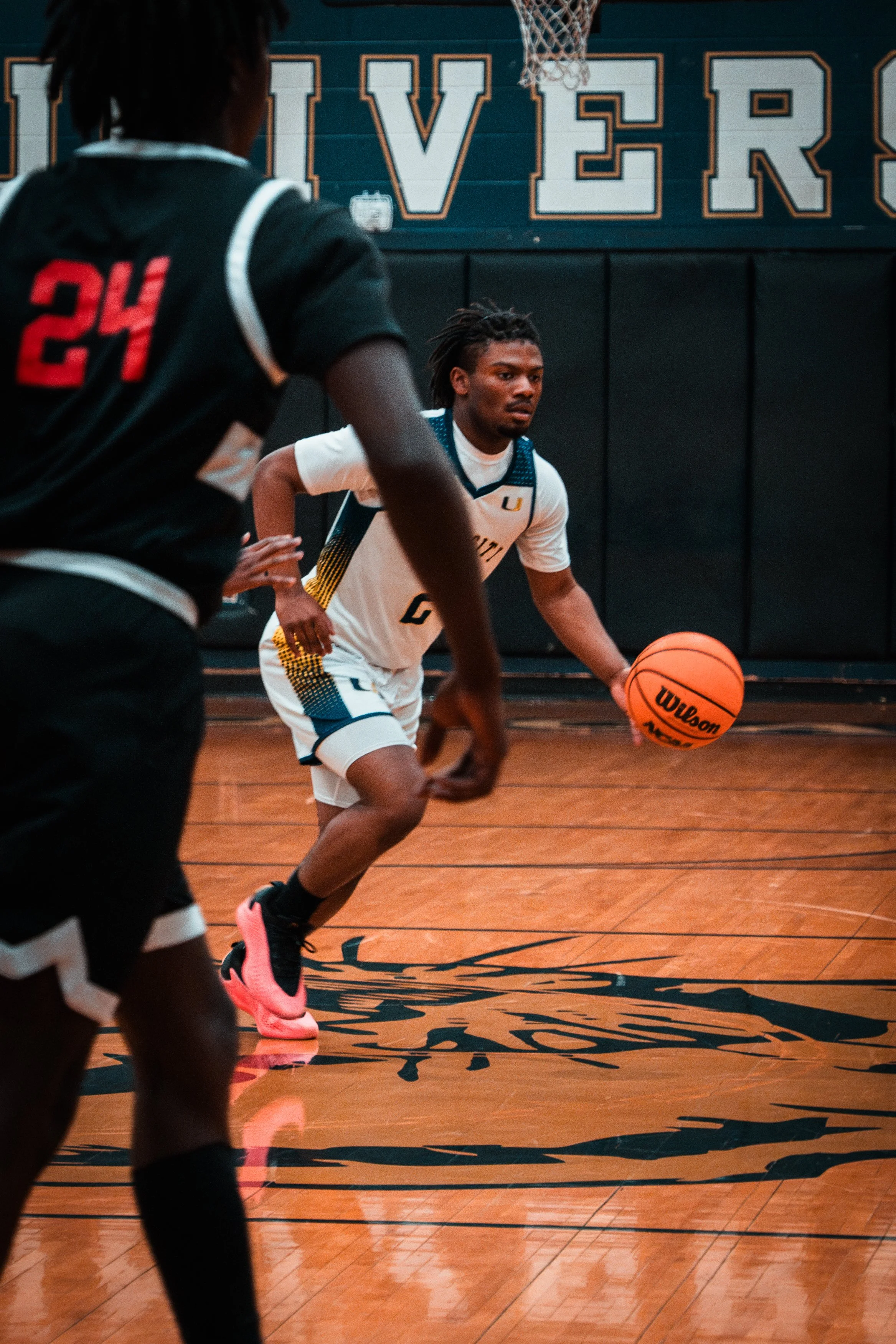 A basketball player dribbling on an indoor court, with another player in the foreground.