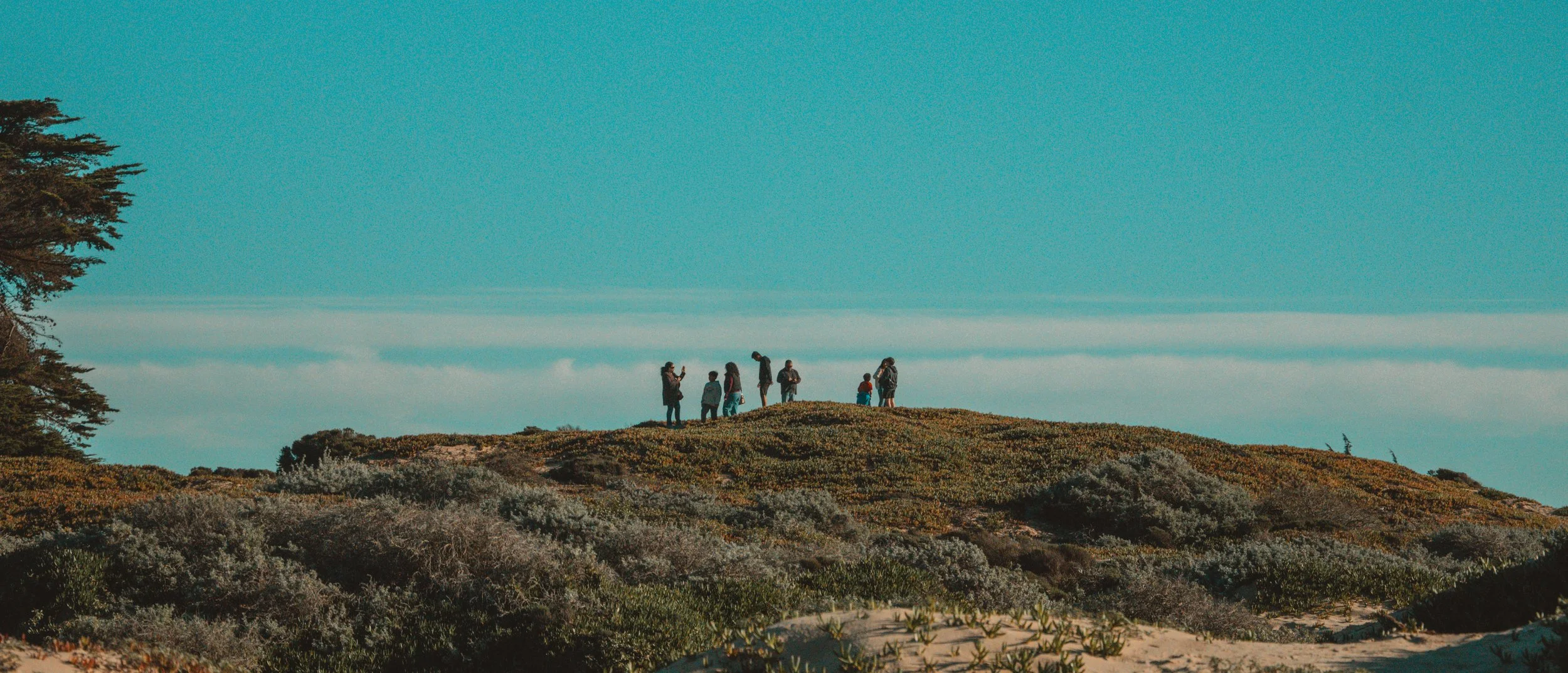 Group of people standing on a hilltop overlooking the landscape under a clear blue sky.