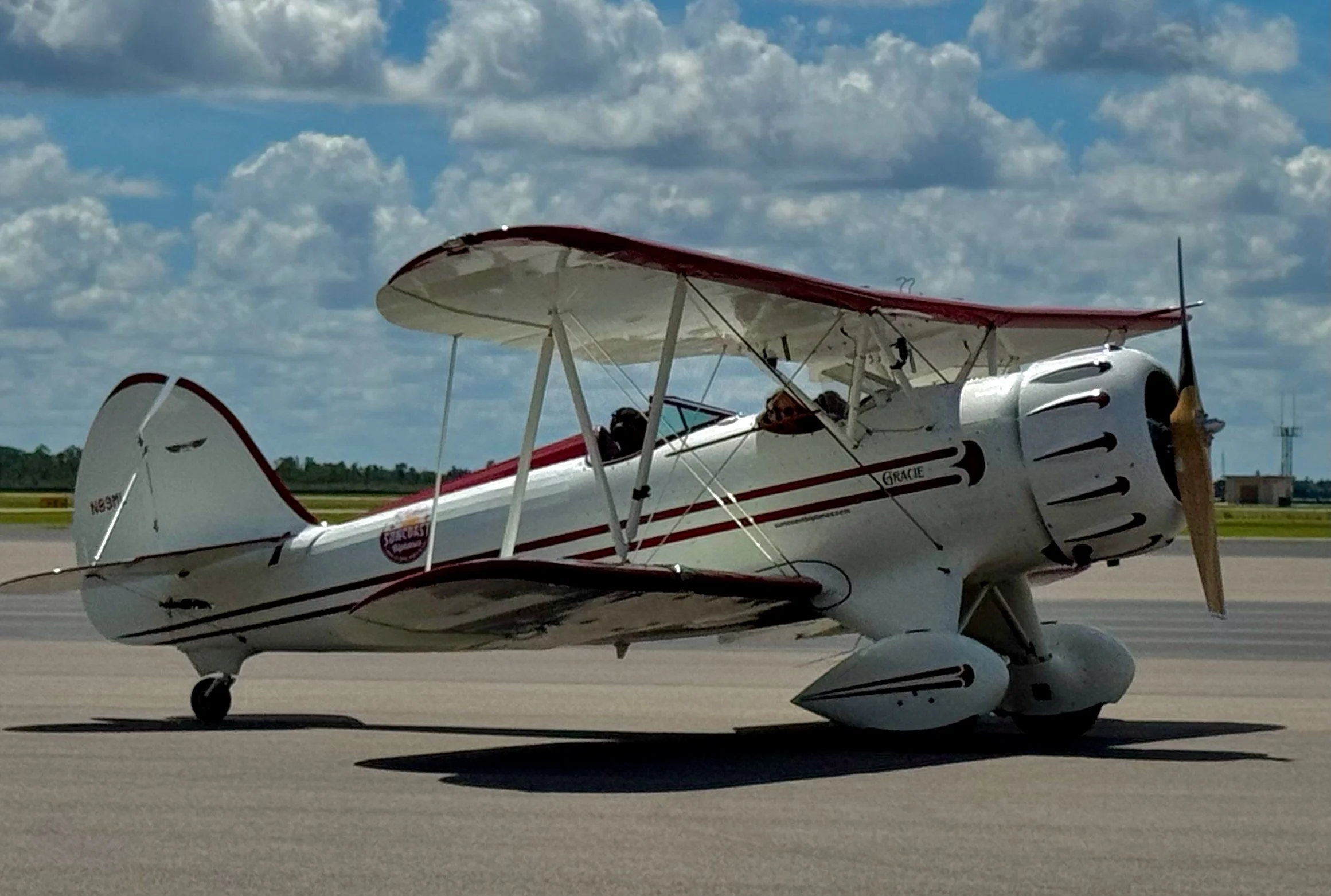 A small white and red biplane with red accents on the wings and tail named Gracie, parked on the PGD airport tarmac, under a partly cloudy sky.
