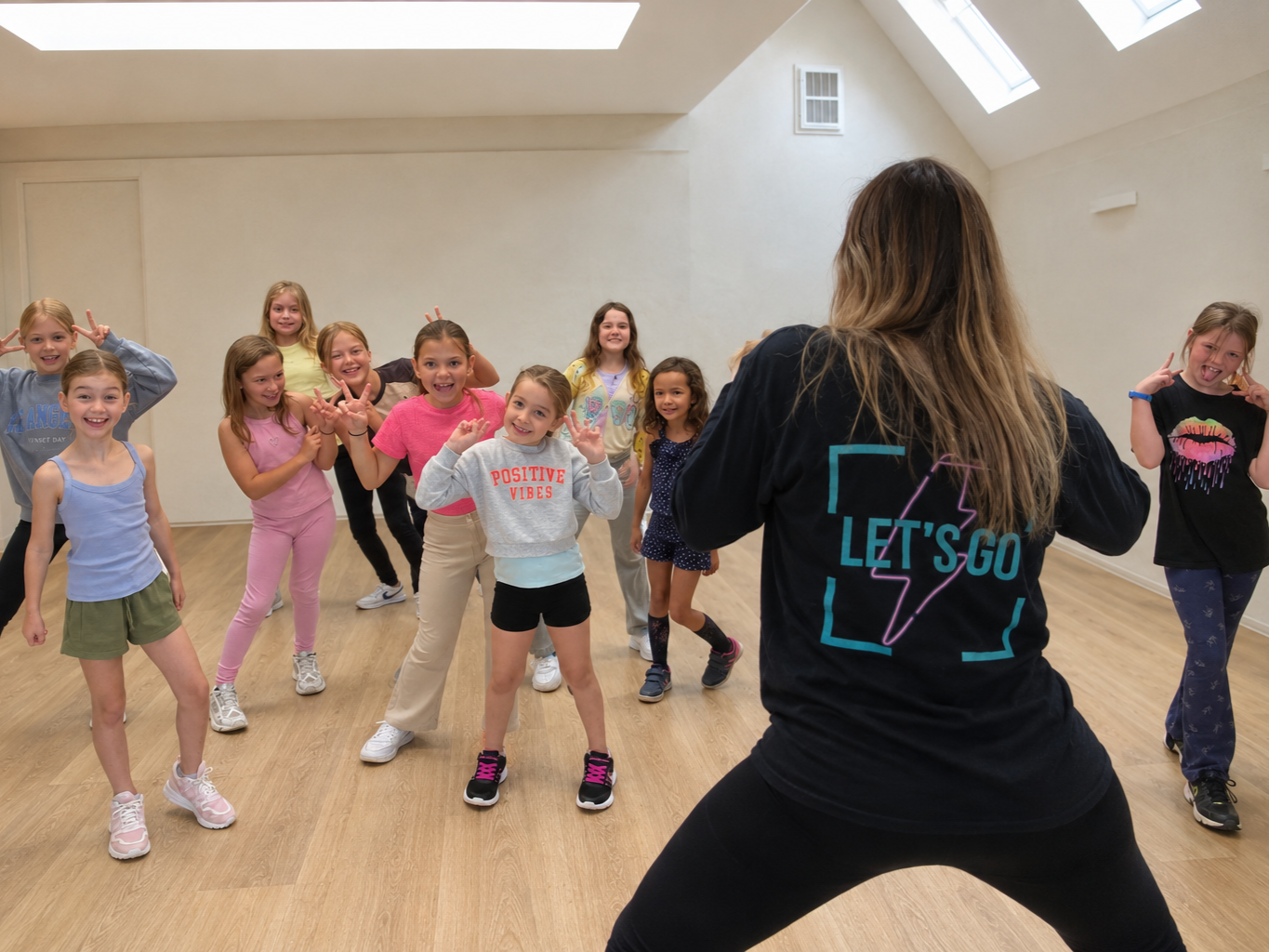 Group of young girls participating in a dance class led by an instructor in a studio with skylights.