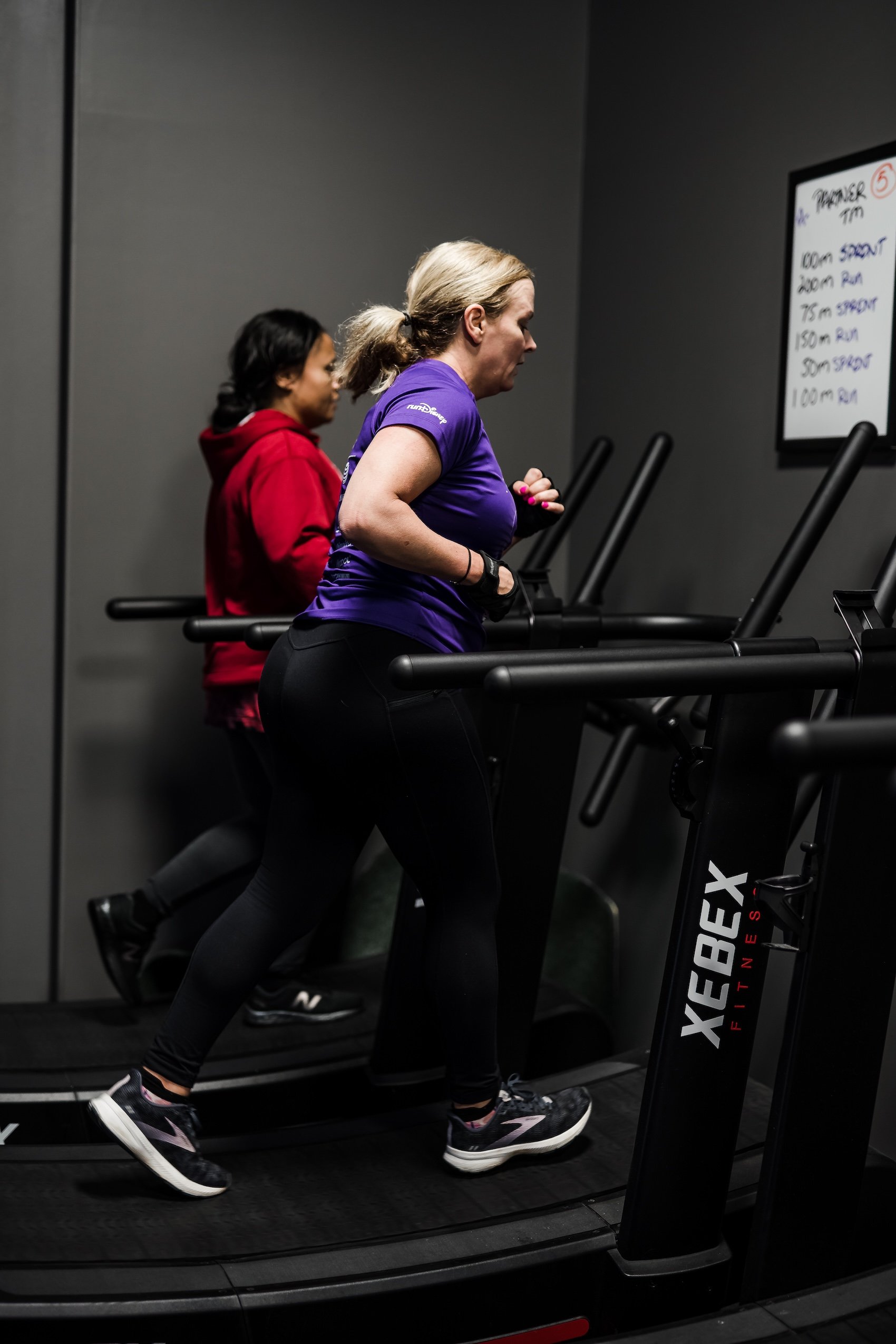 Two women jogging on treadmills in a gym, working out and staying fit.