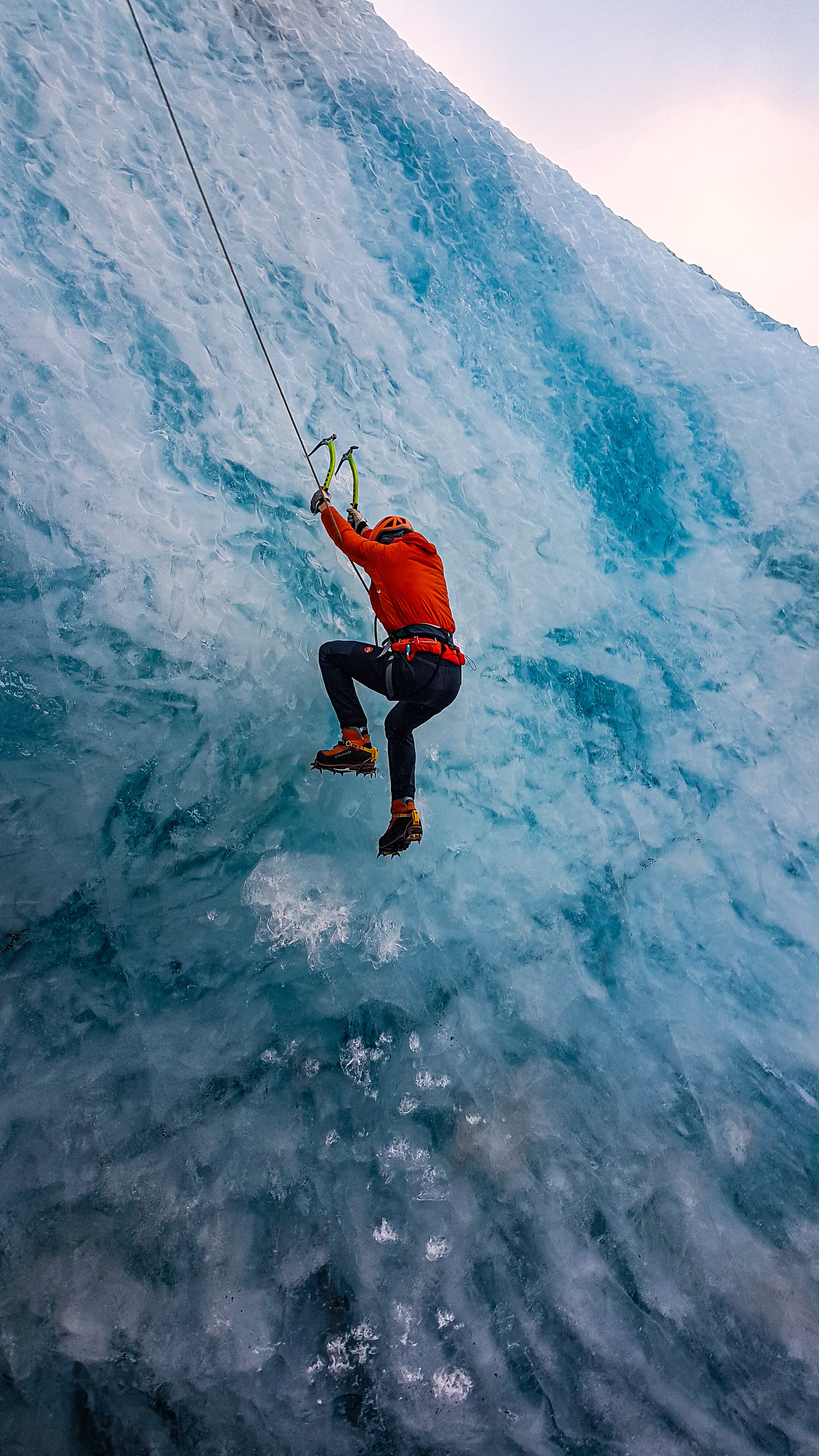 A person in climbing gear rappelling down an ice wall in a glacier.