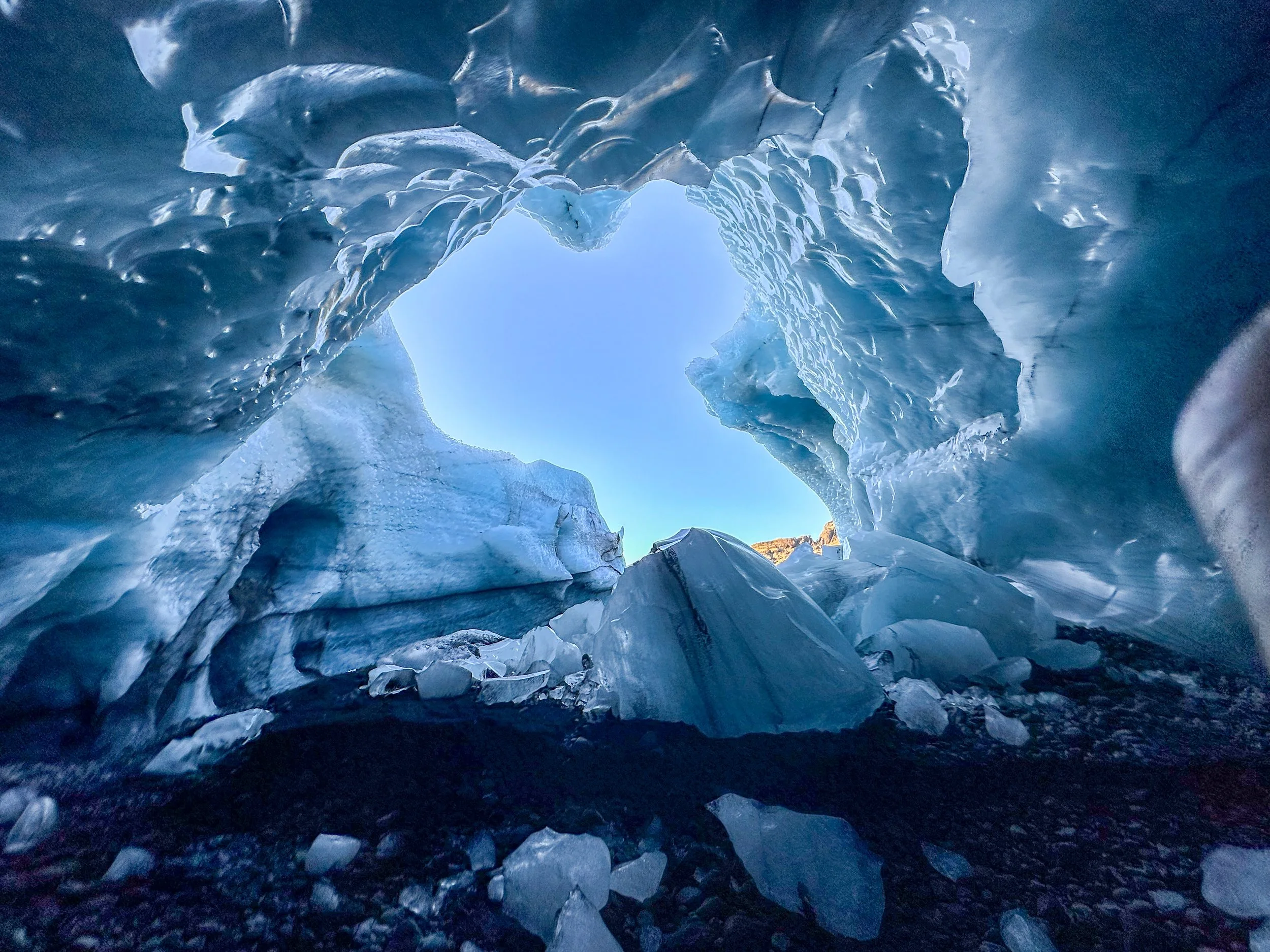 Inside an ice cave with a blue ice ceiling and dark rocks on the ground.