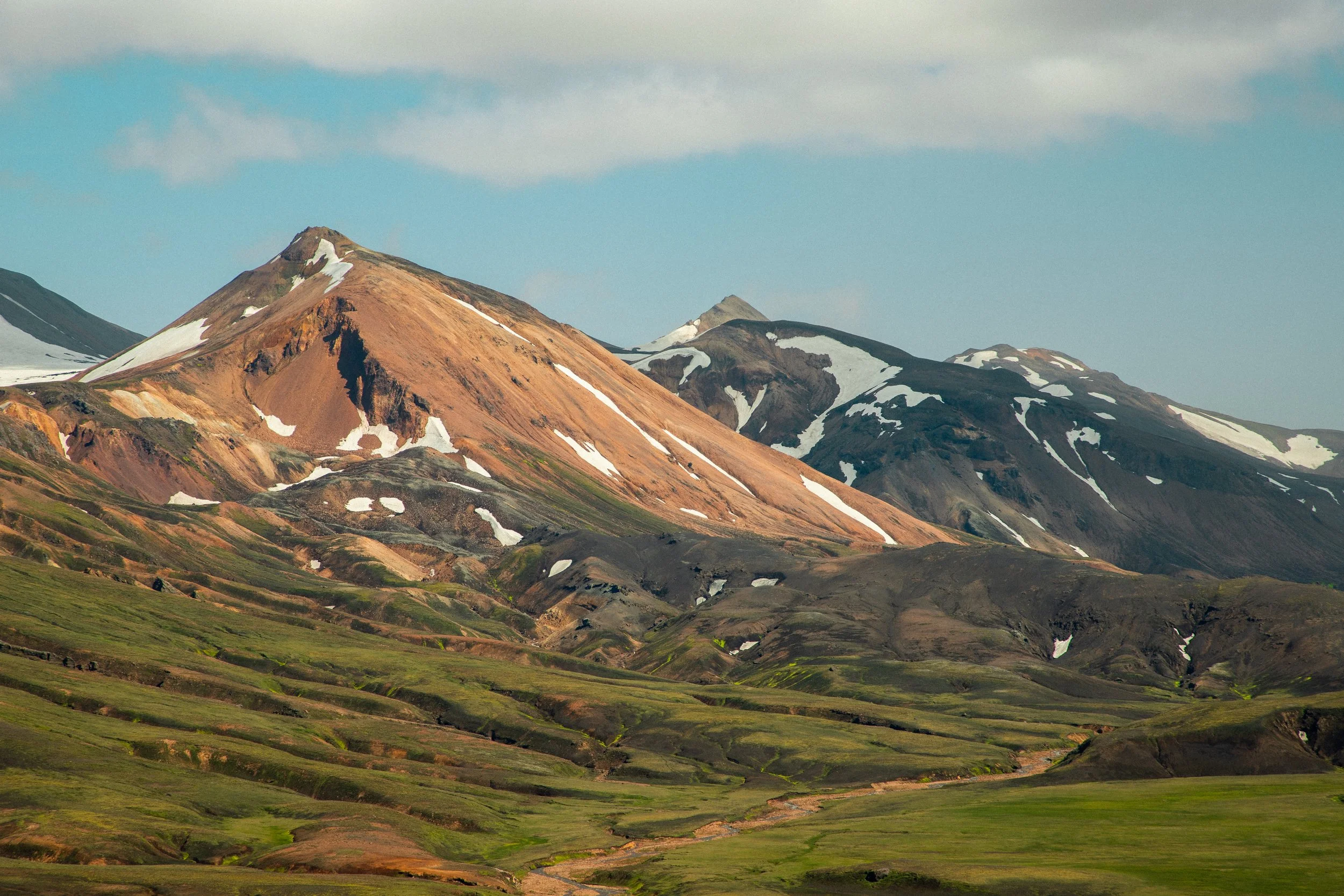 Colorful mountain range with patches of snow and green valleys under a partly cloudy sky.