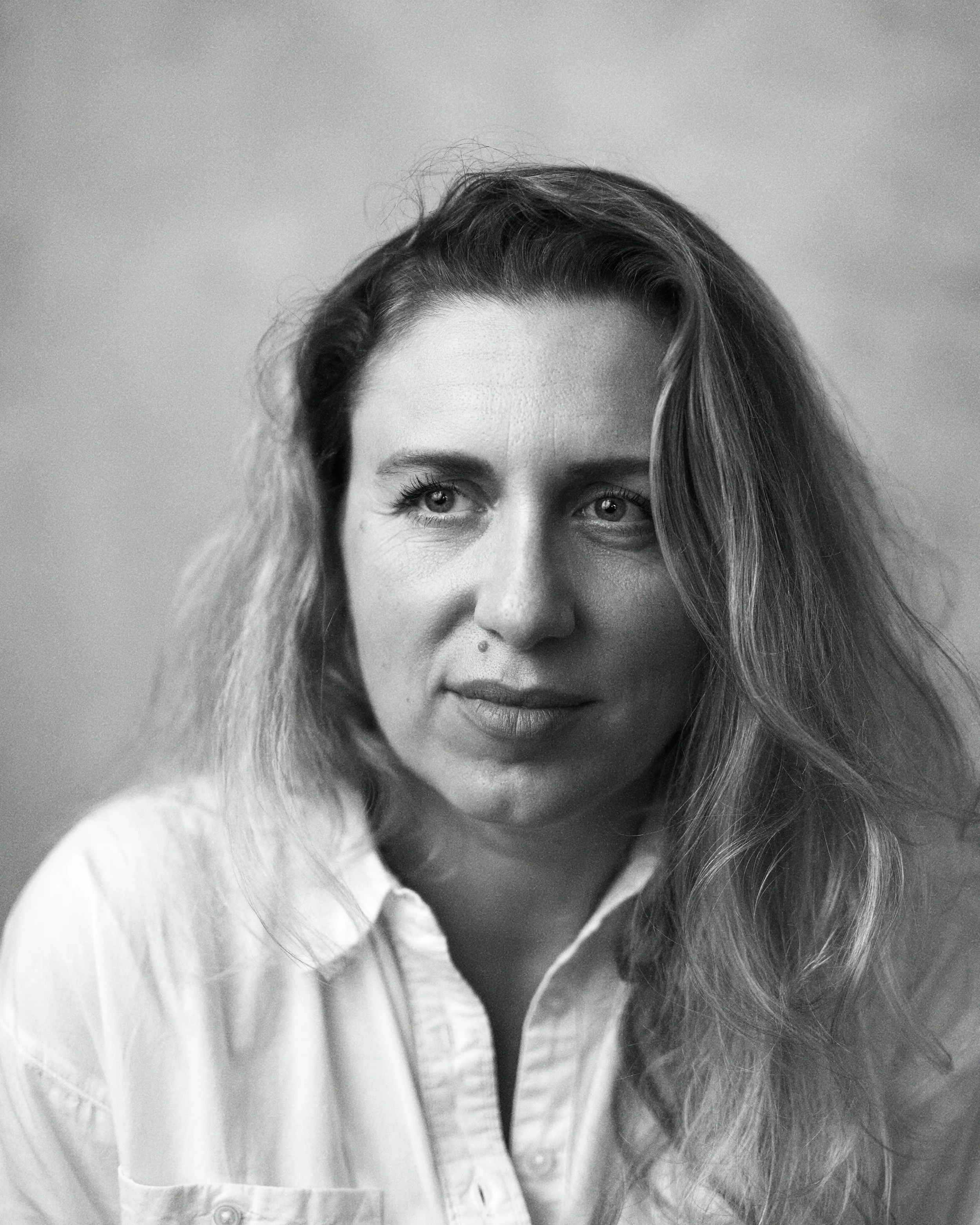 Black and white portrait of a woman with wavy hair, wearing a collared shirt, looking slightly to the side with a neutral expression.